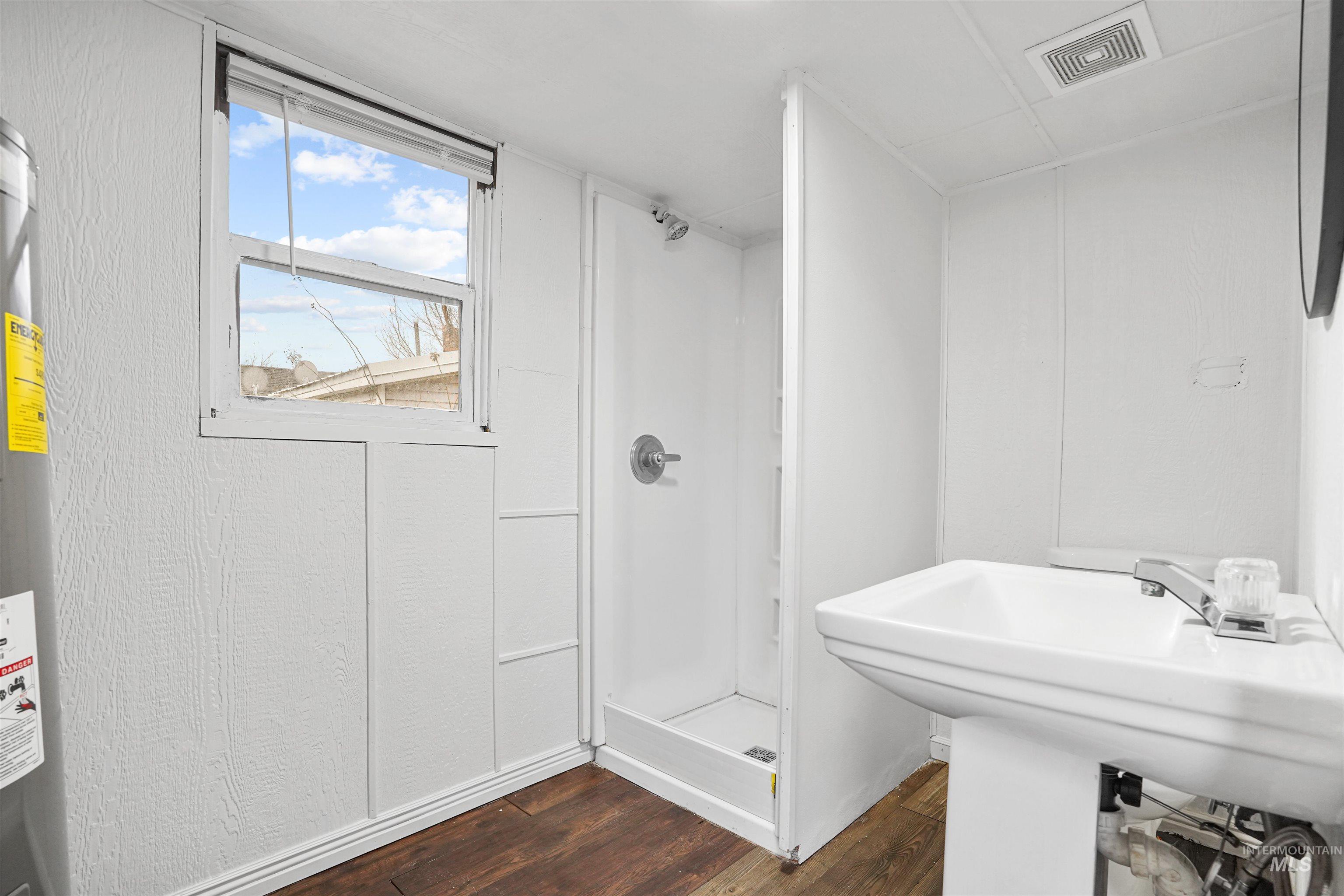 Bathroom with a stall shower, dark wood finished floors, and water heater