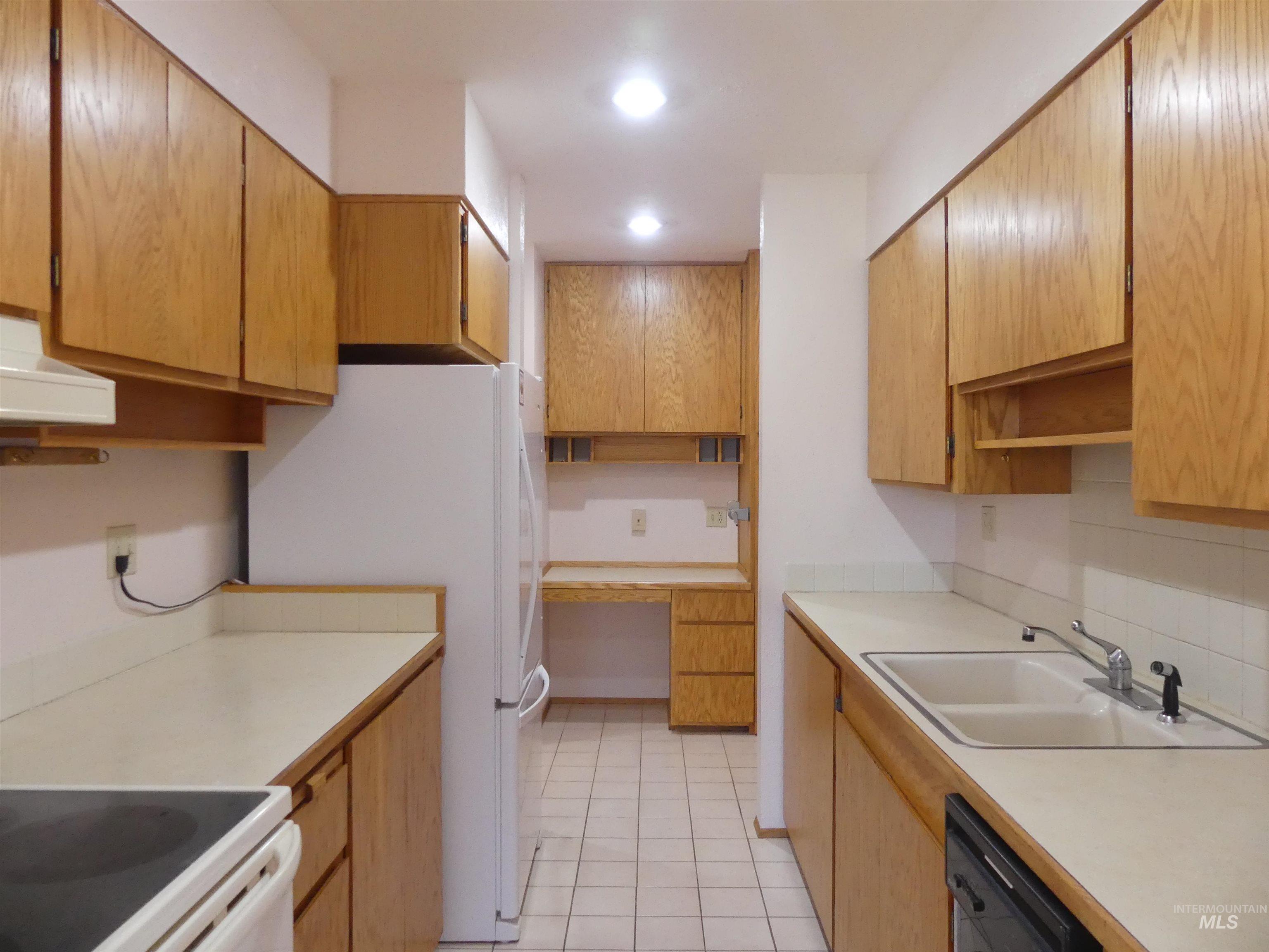Kitchen featuring light countertops, white appliances, light tile patterned floors, brown cabinets, and recessed lighting