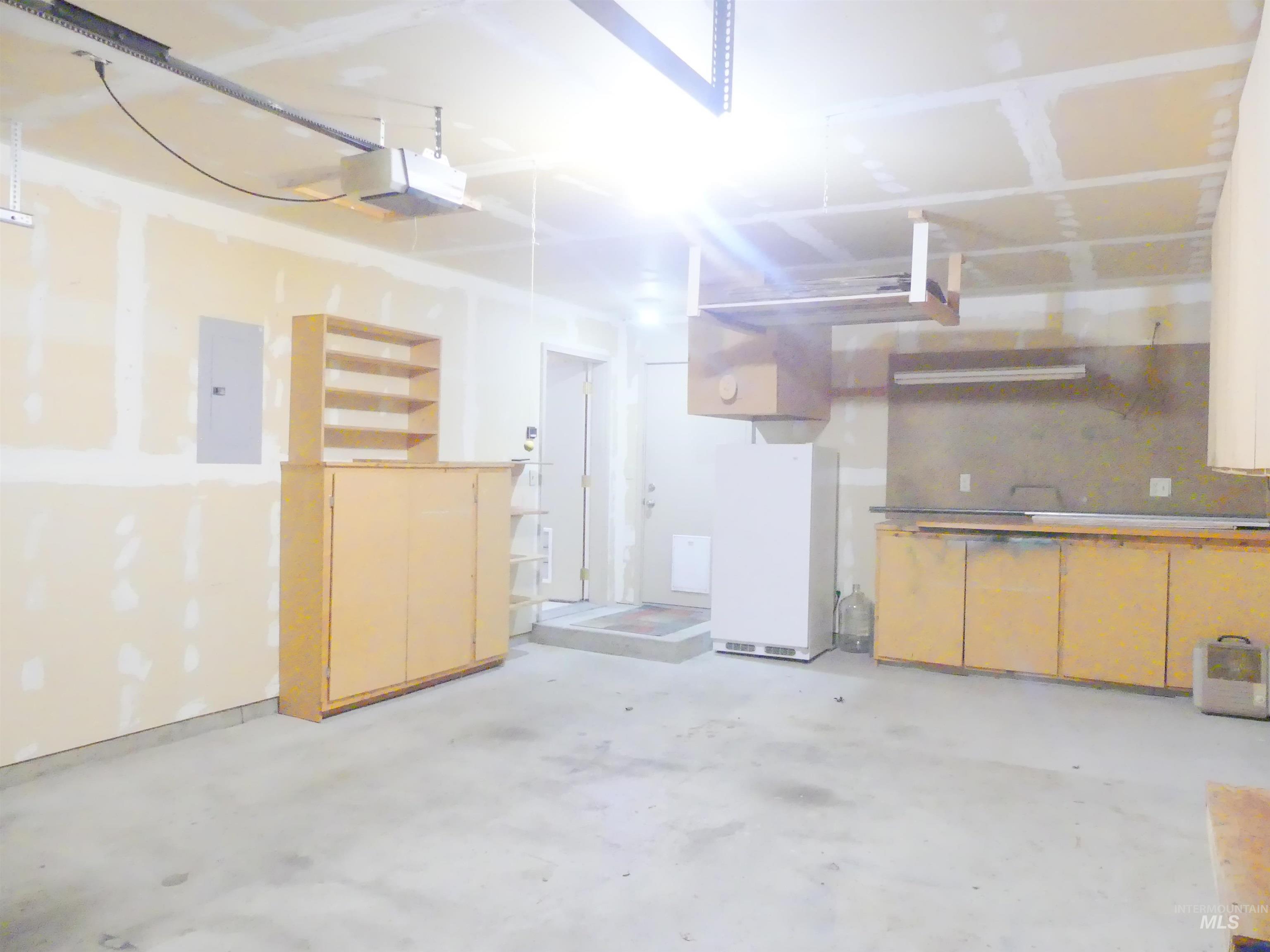 Garage with freestanding refrigerator, electric panel, and a garage door opener