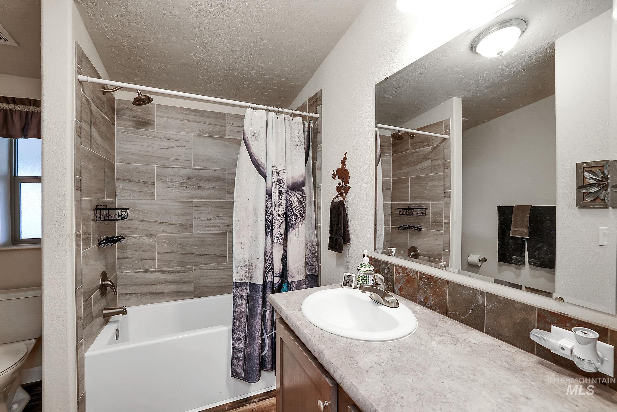 Bathroom with shower / tub combo, vanity, and a textured ceiling
