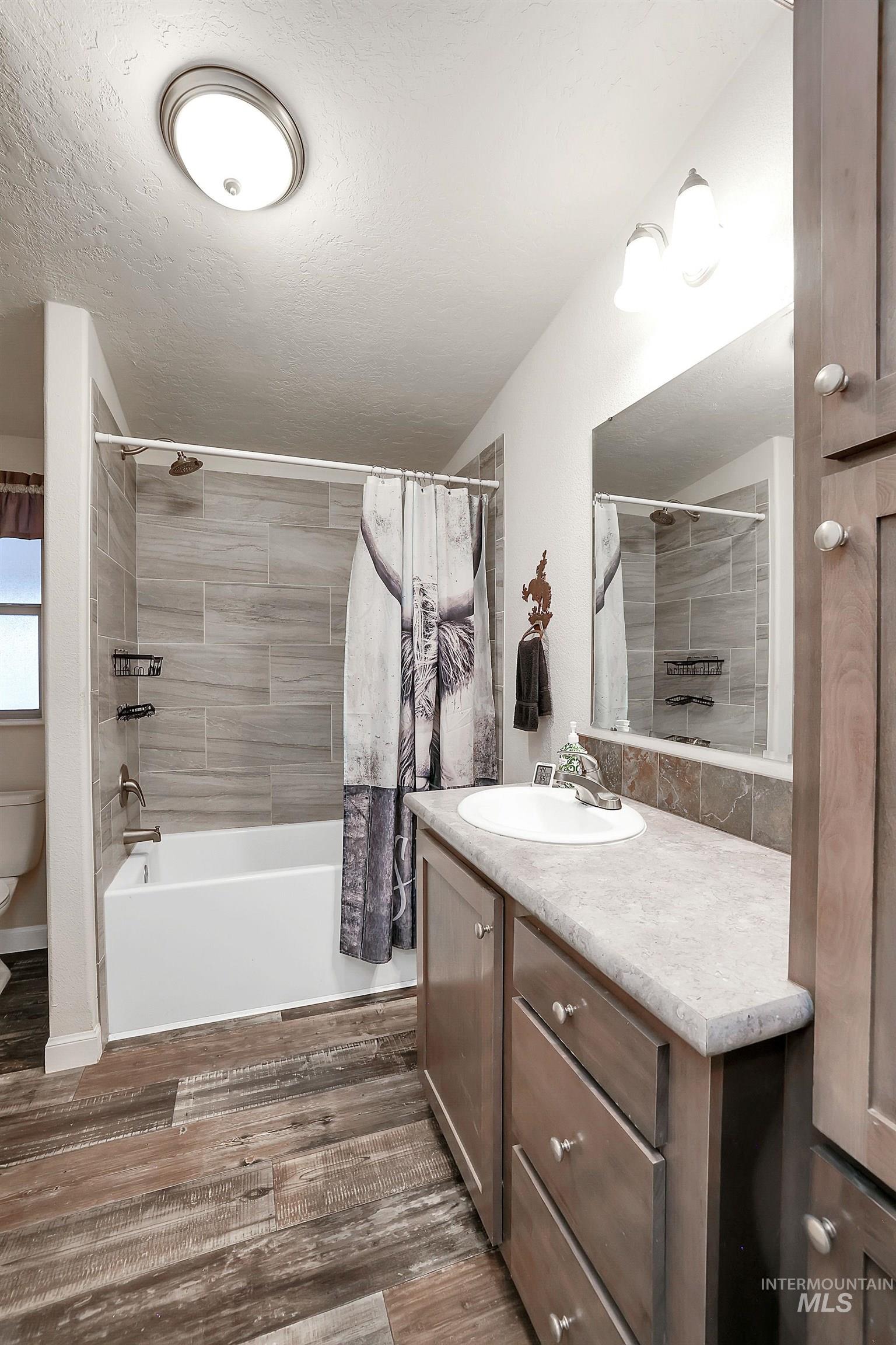 Bathroom with vanity, shower / tub combo, dark wood-type flooring, and a textured ceiling