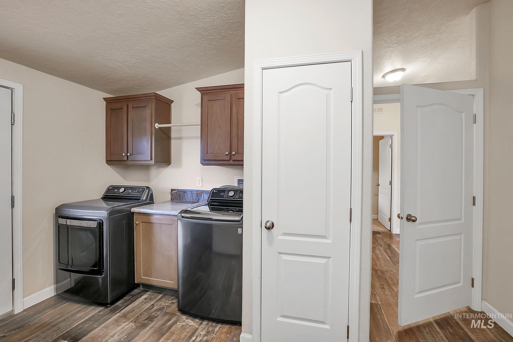 Laundry room featuring a textured ceiling, dark wood-type flooring, cabinet space, and separate washer and dryer