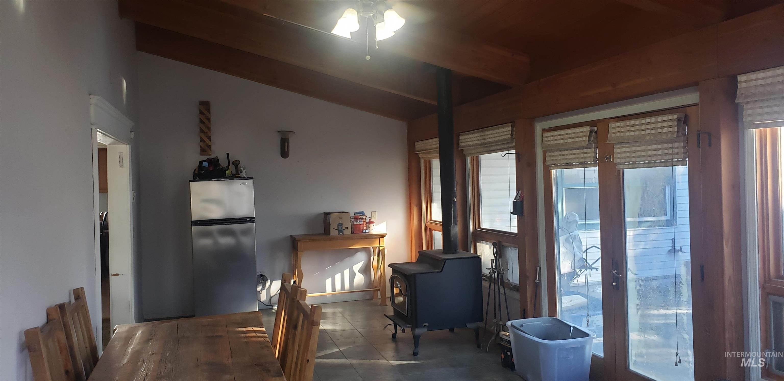 Dining area with a wood stove, a ceiling fan, tile patterned flooring, and beamed ceiling