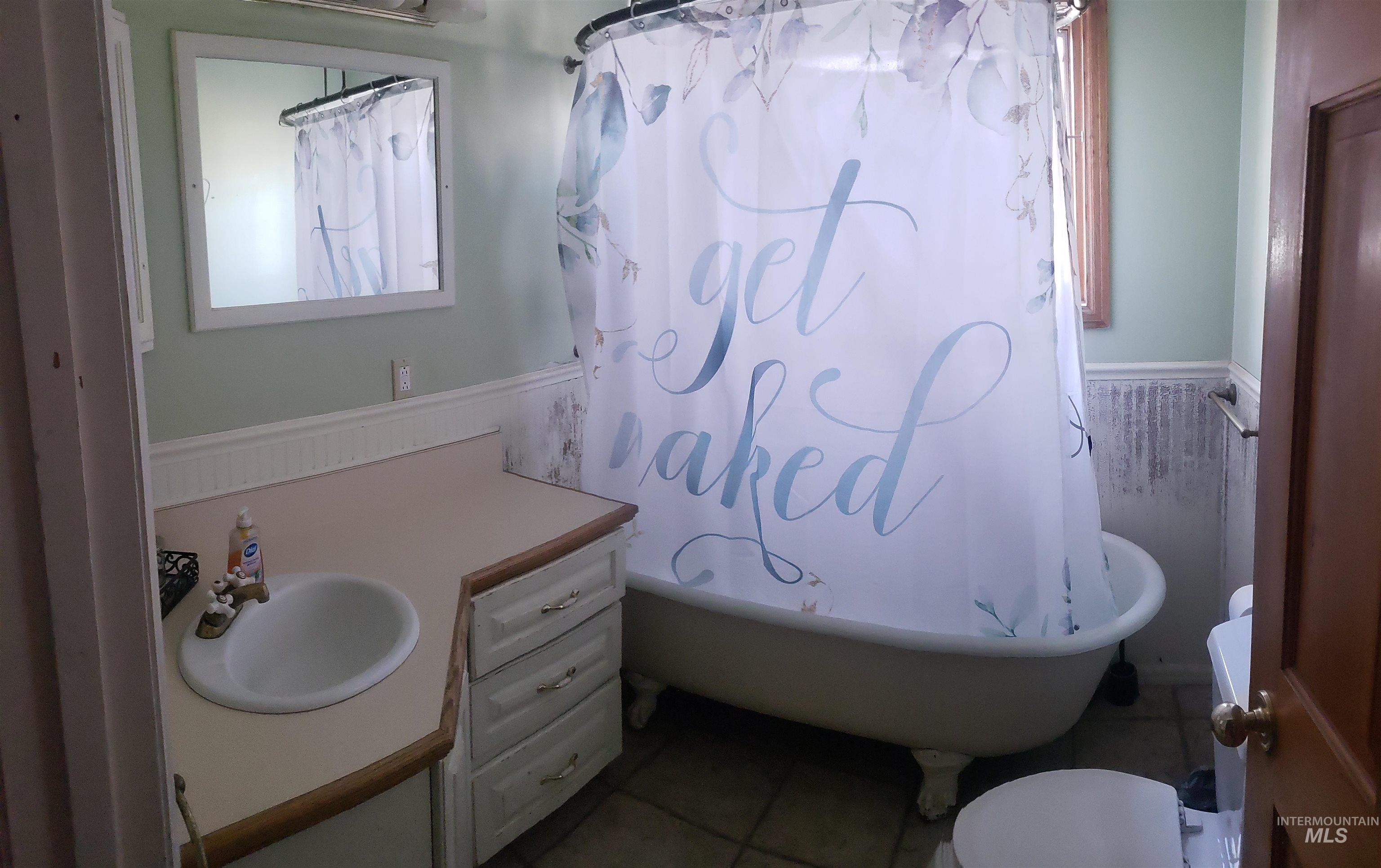 Full bathroom featuring a wainscoted wall, vanity, tile patterned flooring, and shower / bath combo