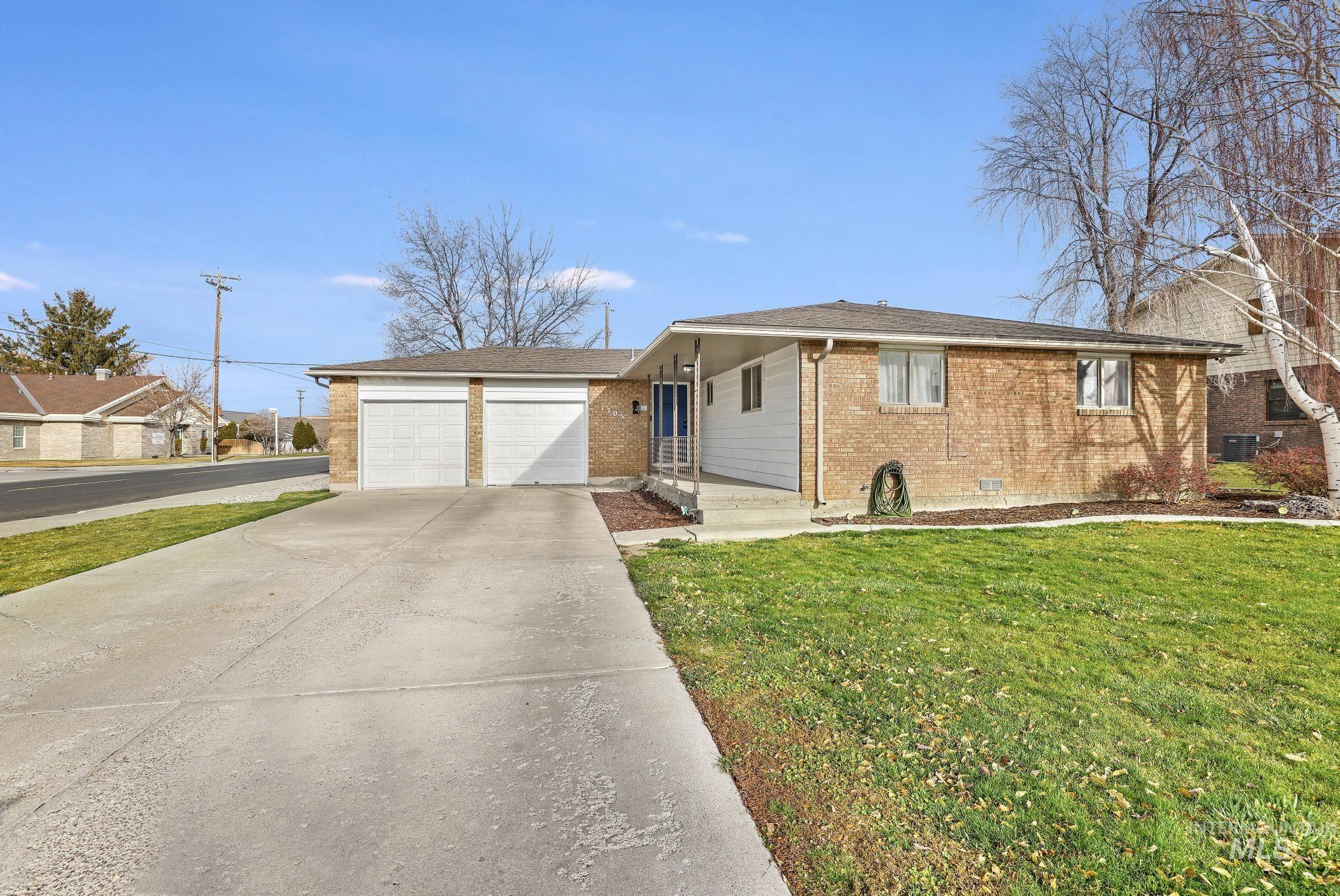 Ranch-style house featuring brick siding, concrete driveway, a front lawn, an attached garage, and a shingled roof