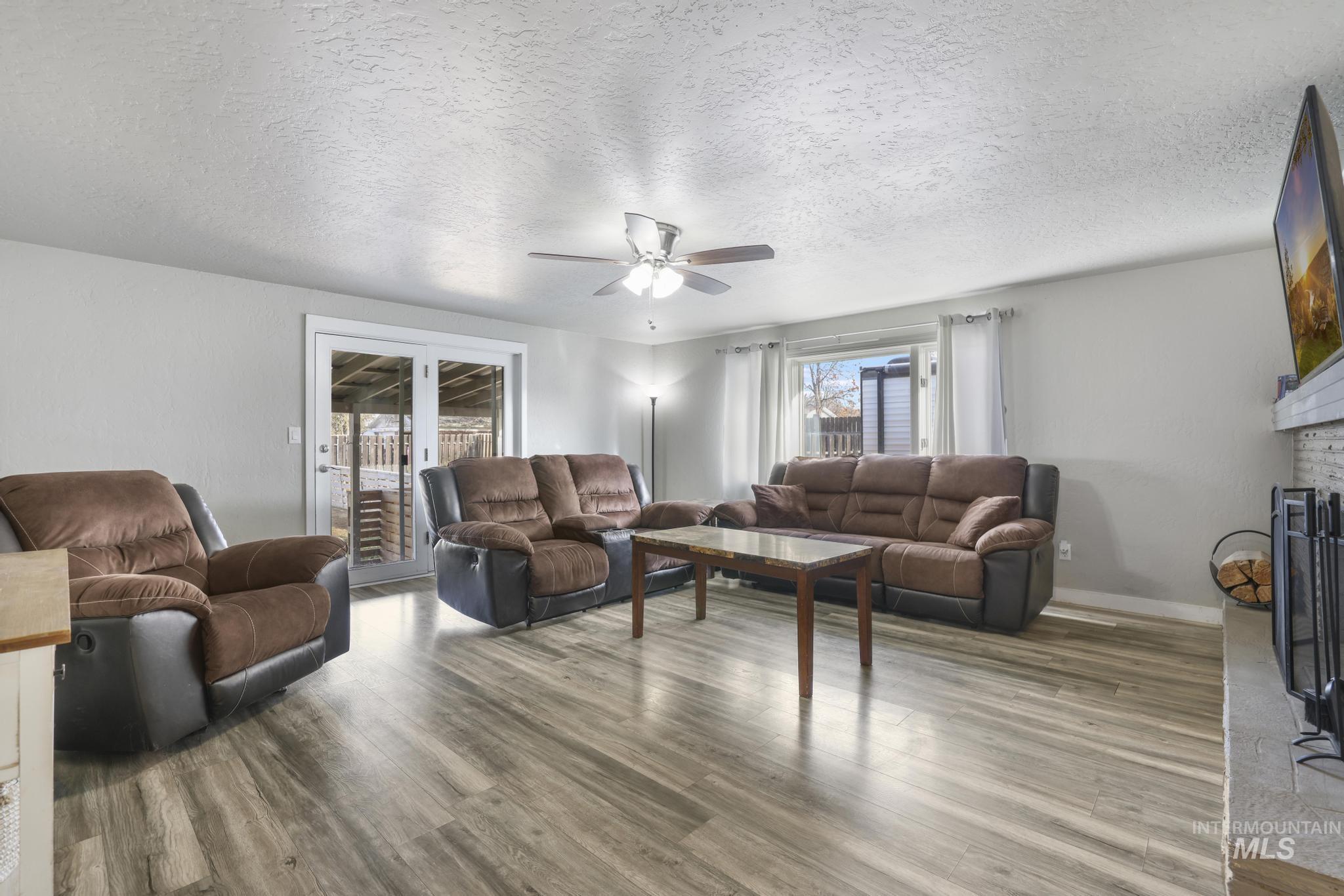 Living room featuring a textured ceiling, a brick fireplace, ceiling fan, wood finished floors, and french doors