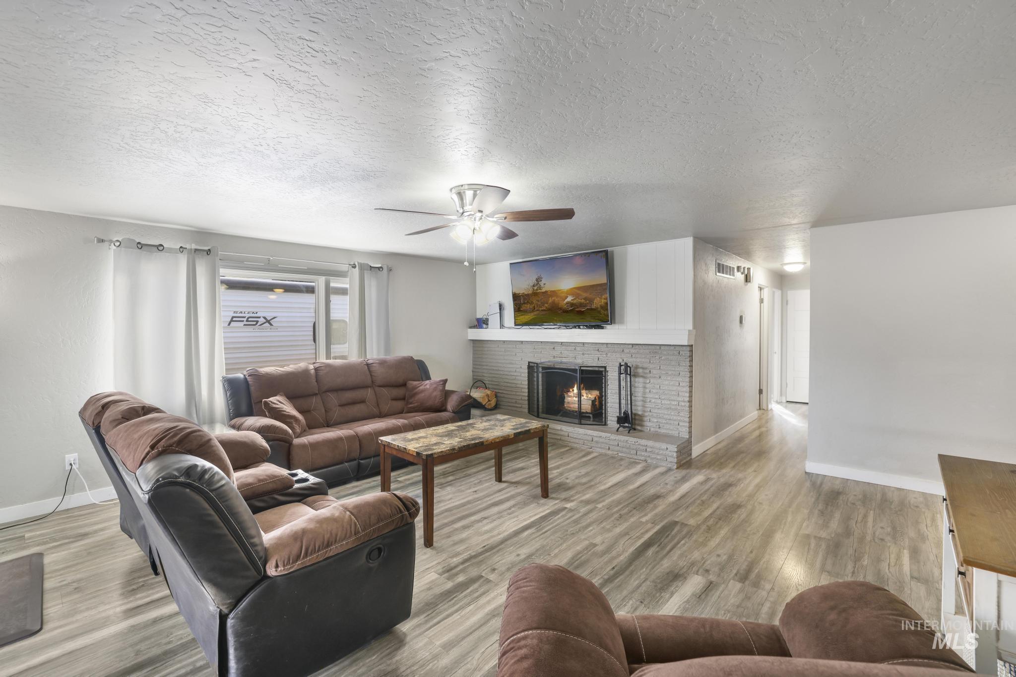 Living room with a textured ceiling, a fireplace, ceiling fan, and light wood finished floors