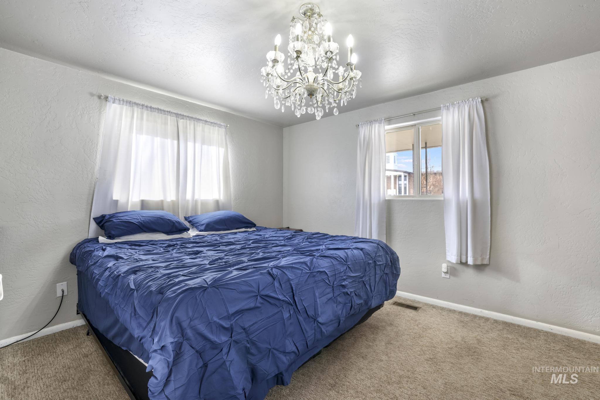 Carpeted bedroom with a textured wall, a chandelier, and a textured ceiling