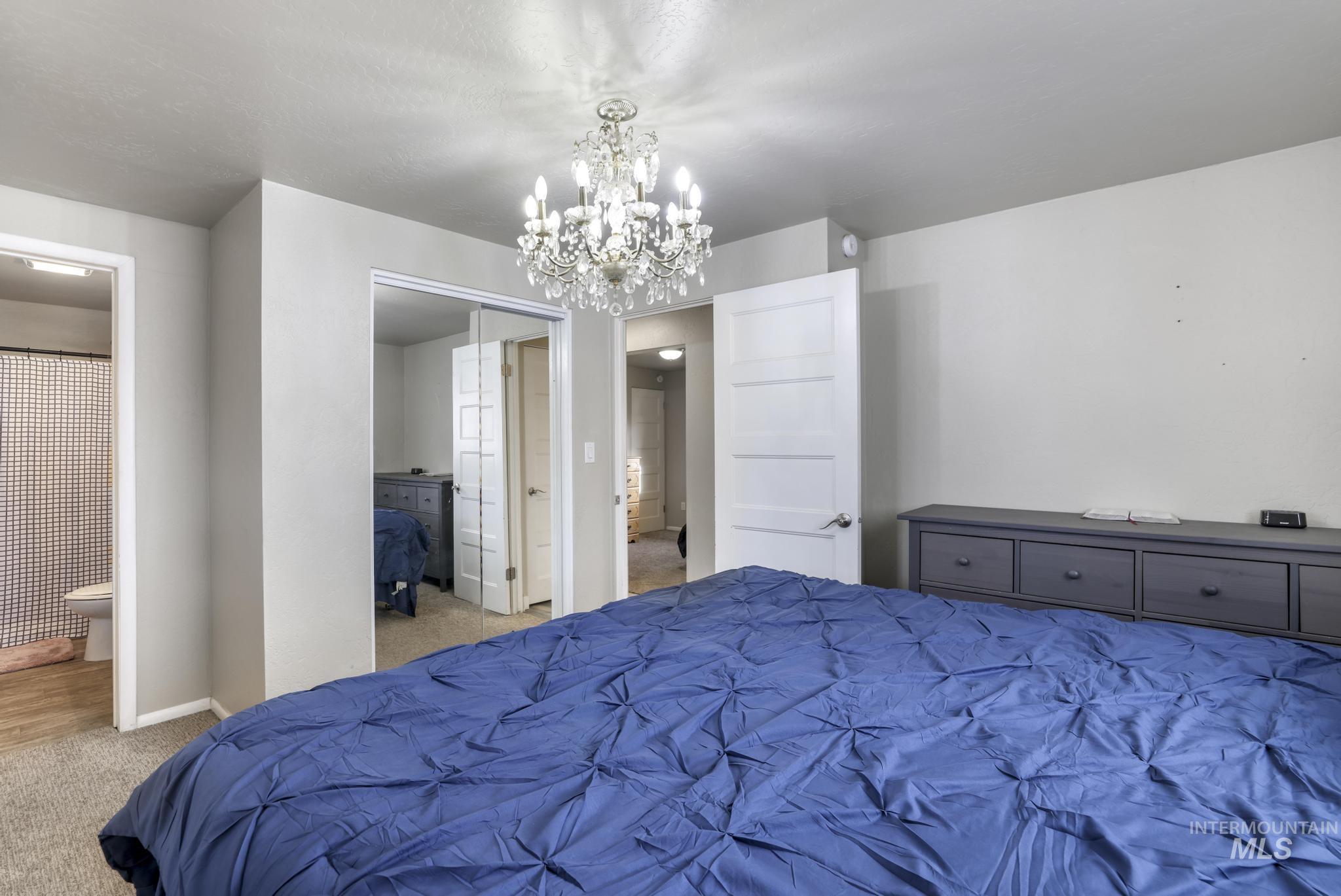 Carpeted bedroom with a chandelier, ensuite bathroom, and a closet