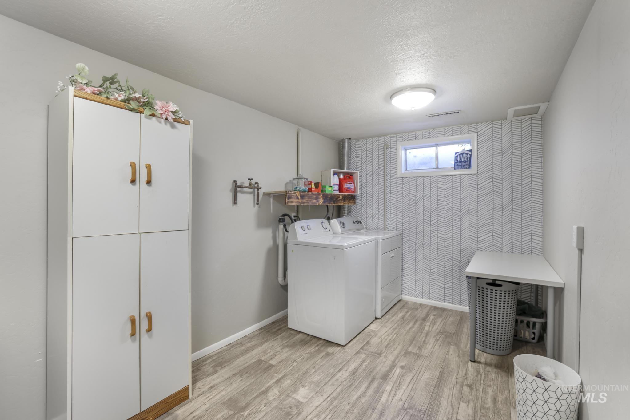 Laundry area featuring a textured ceiling, light wood-style floors, washer and dryer, an accent wall, and wallpapered walls