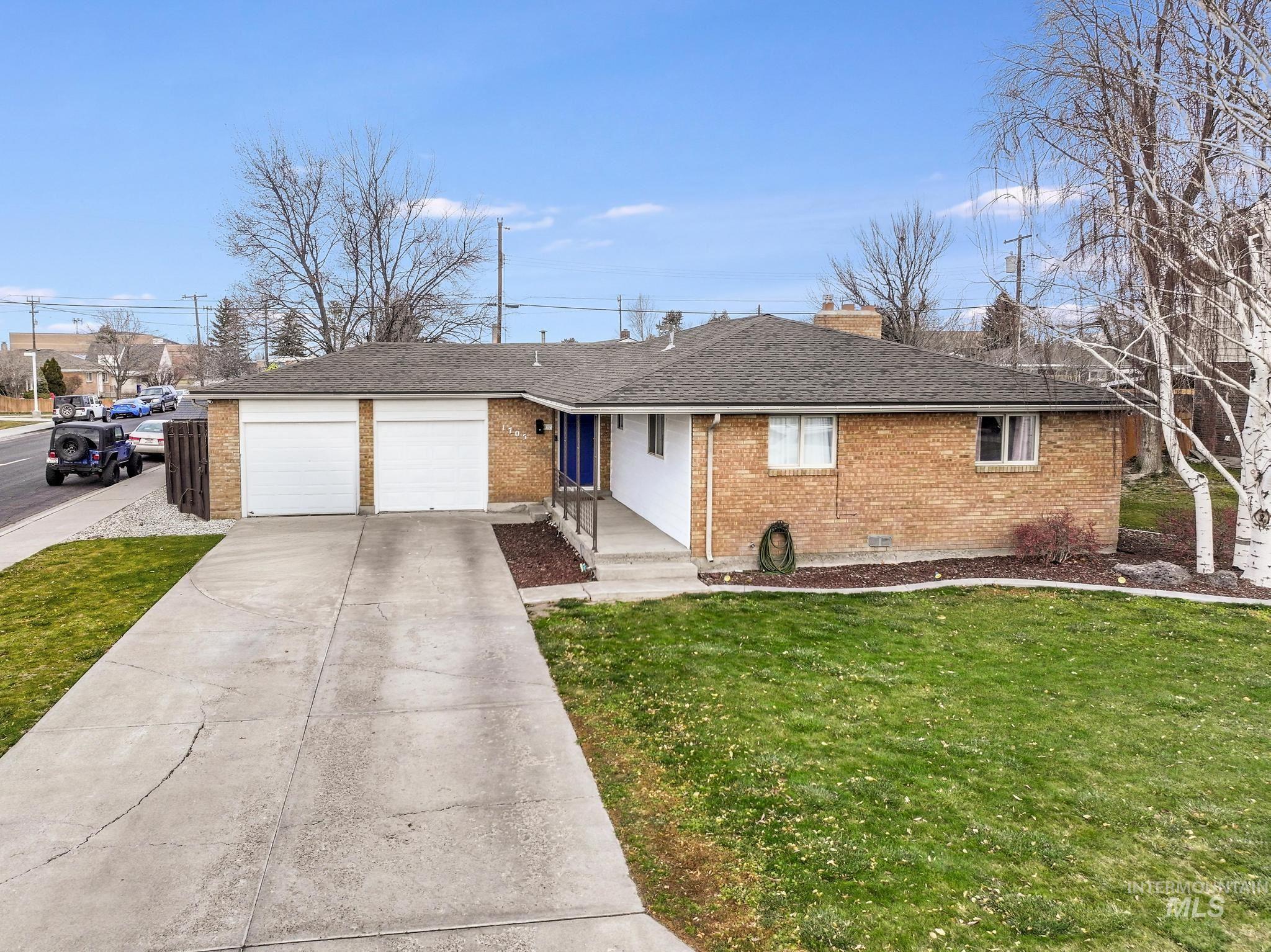 Ranch-style home featuring brick siding, a front yard, roof with shingles, and a garage