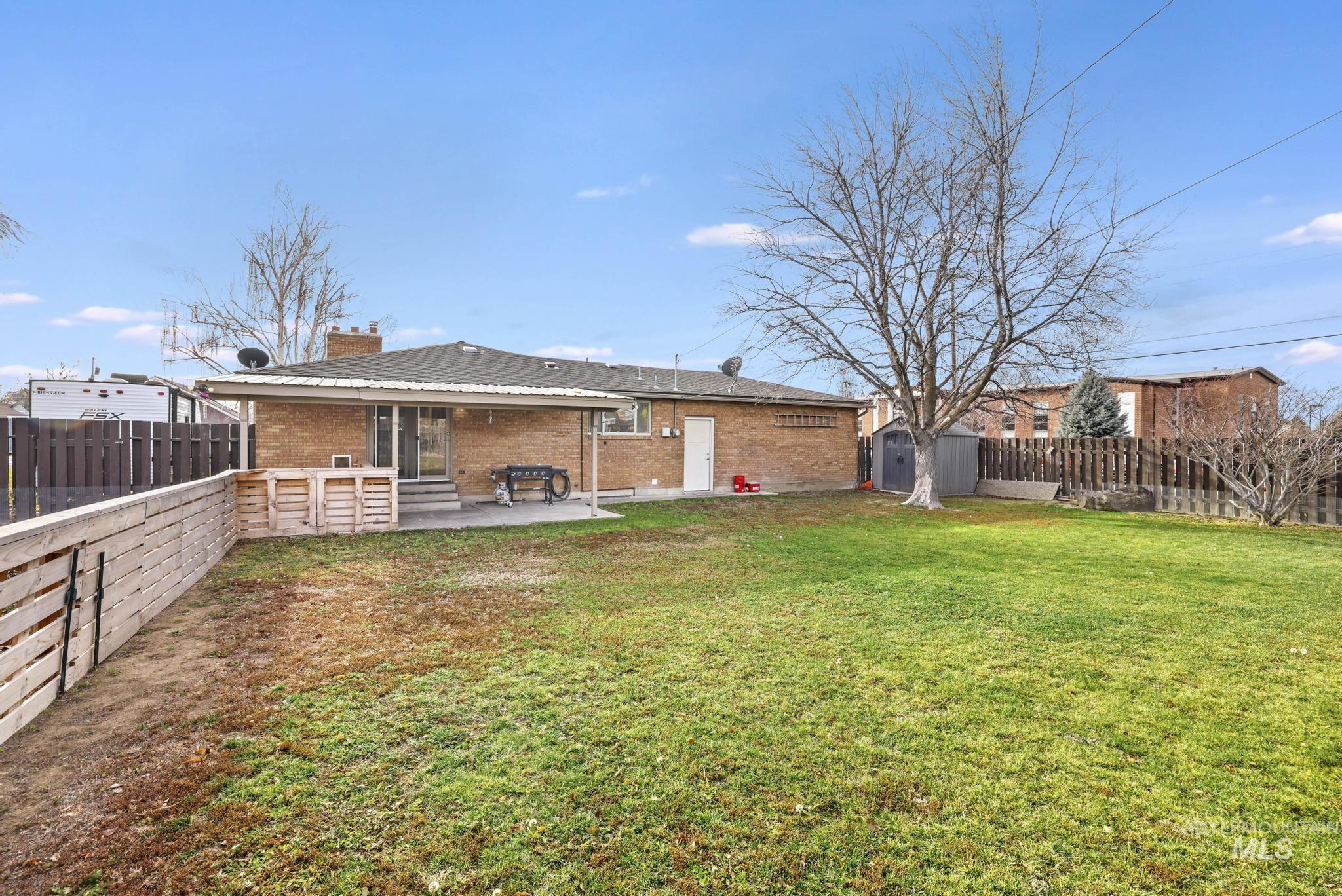 Rear view of house featuring a shed, brick siding, a fenced backyard, and a patio area