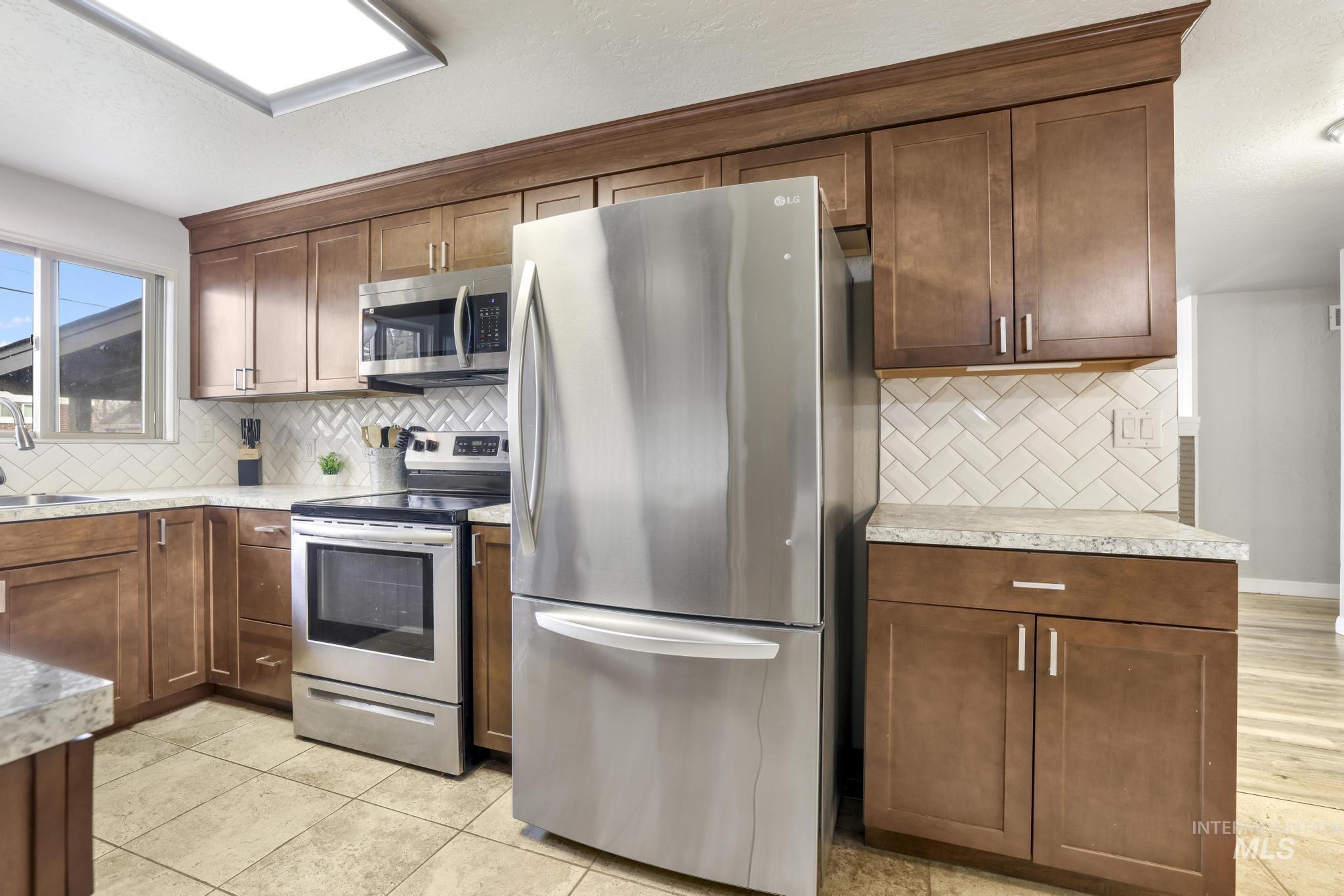 Kitchen with stainless steel appliances, tasteful backsplash, a textured ceiling, and brown cabinetry