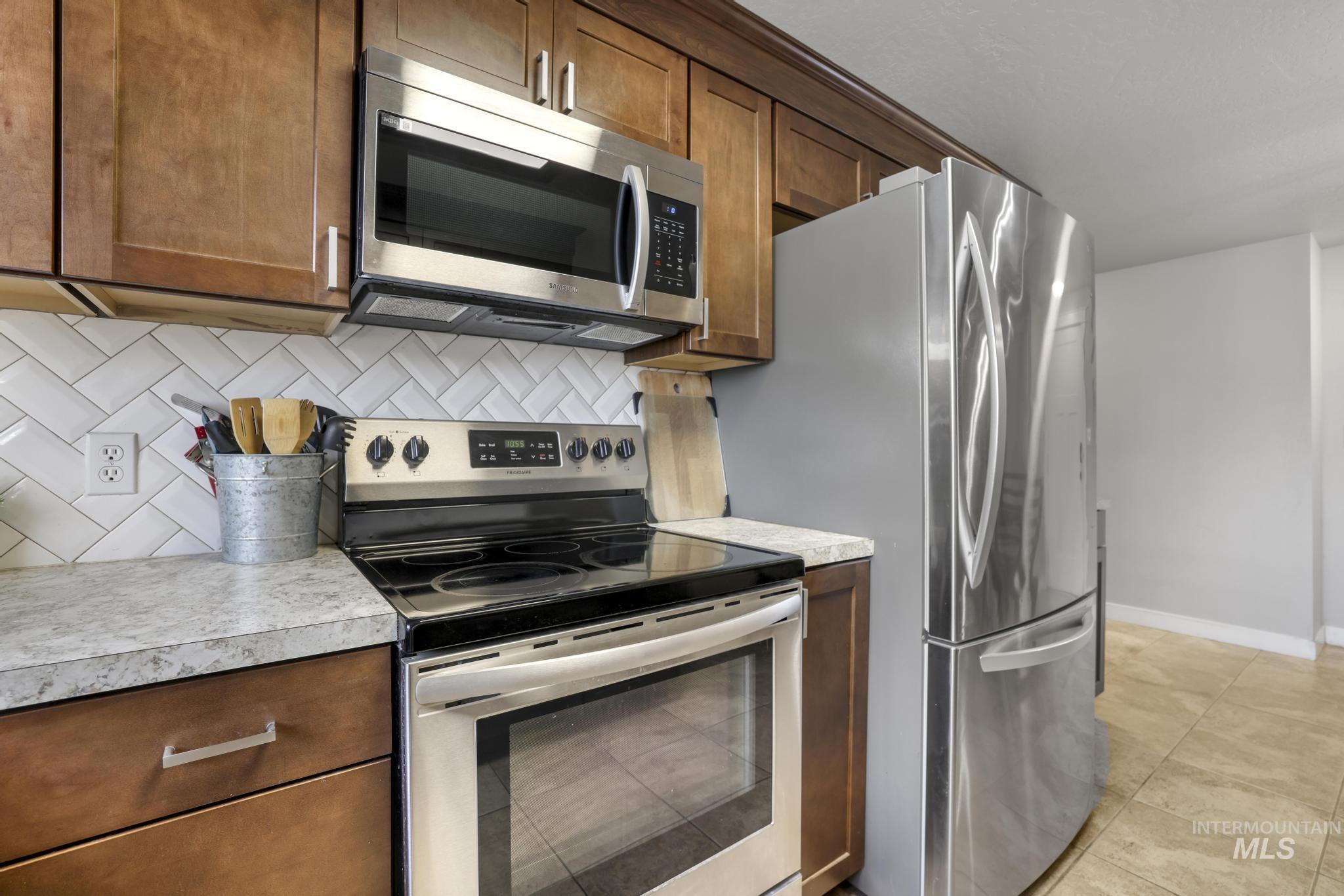 Kitchen featuring stainless steel appliances, backsplash, light countertops, and brown cabinets