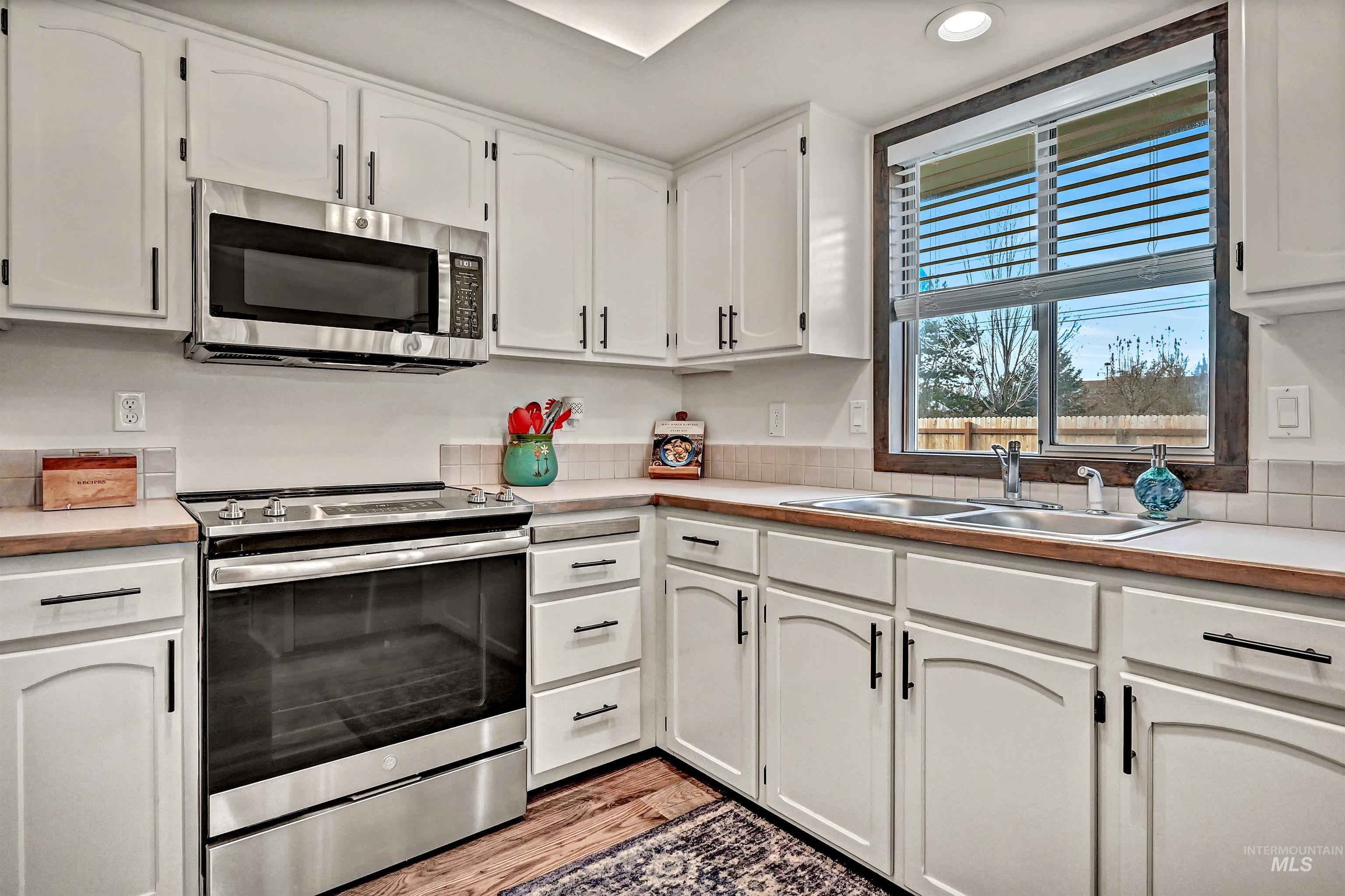 Kitchen with stainless steel appliances, light countertops, white cabinets, and light wood-style flooring