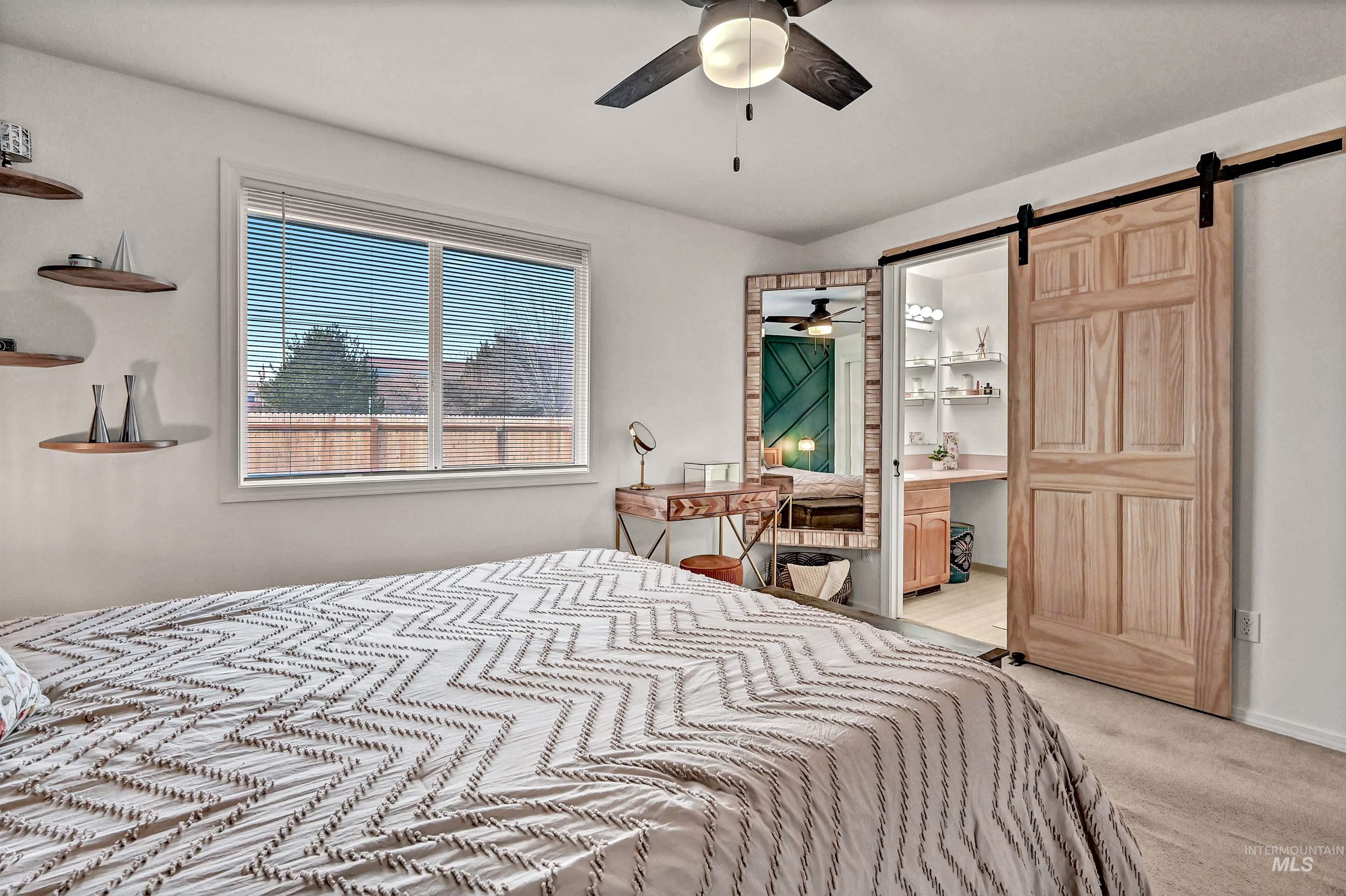 Bedroom featuring connected bathroom, a barn door, light carpet, and a ceiling fan