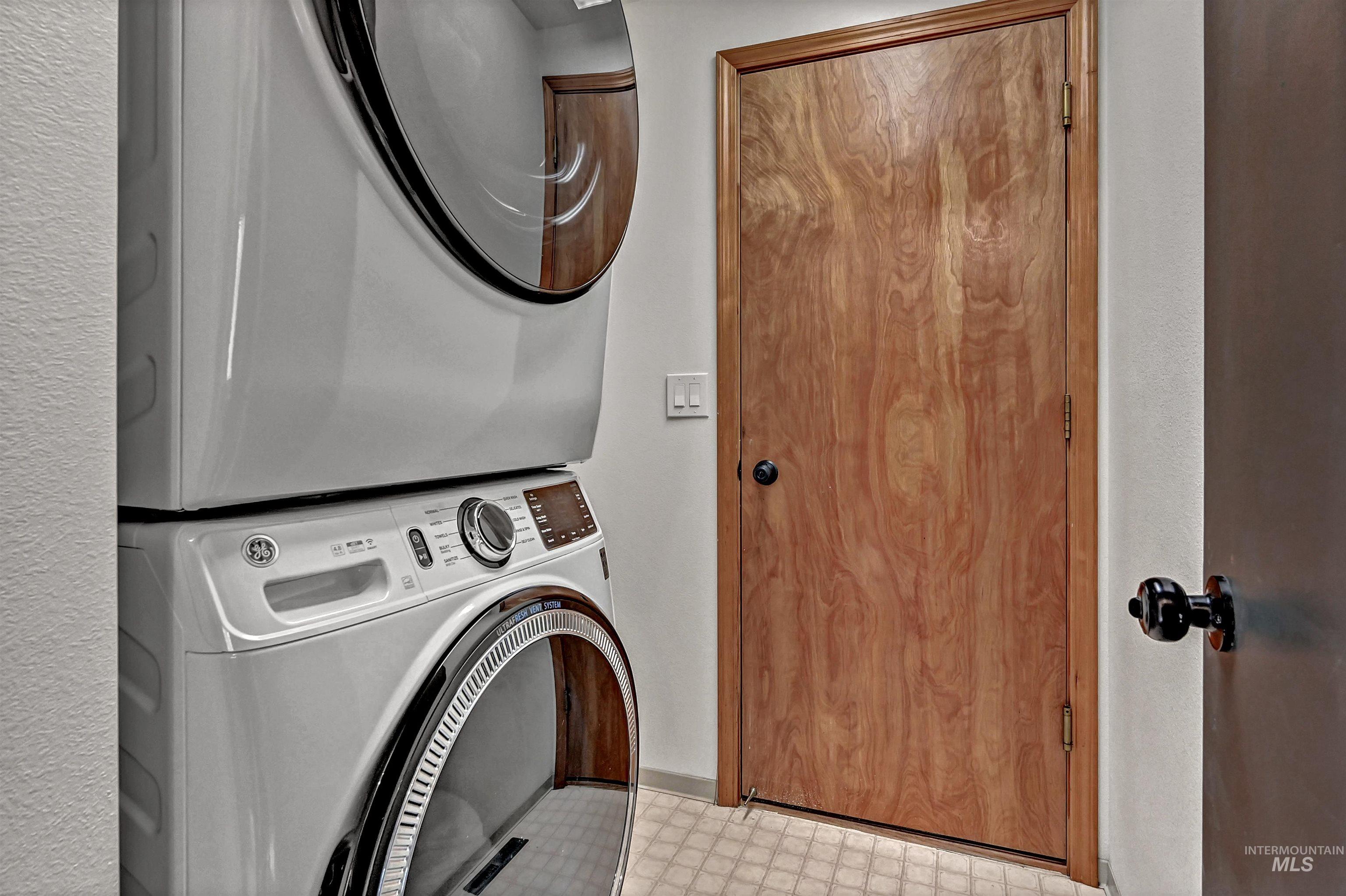 Laundry area featuring light floors and stacked washing machine and dryer