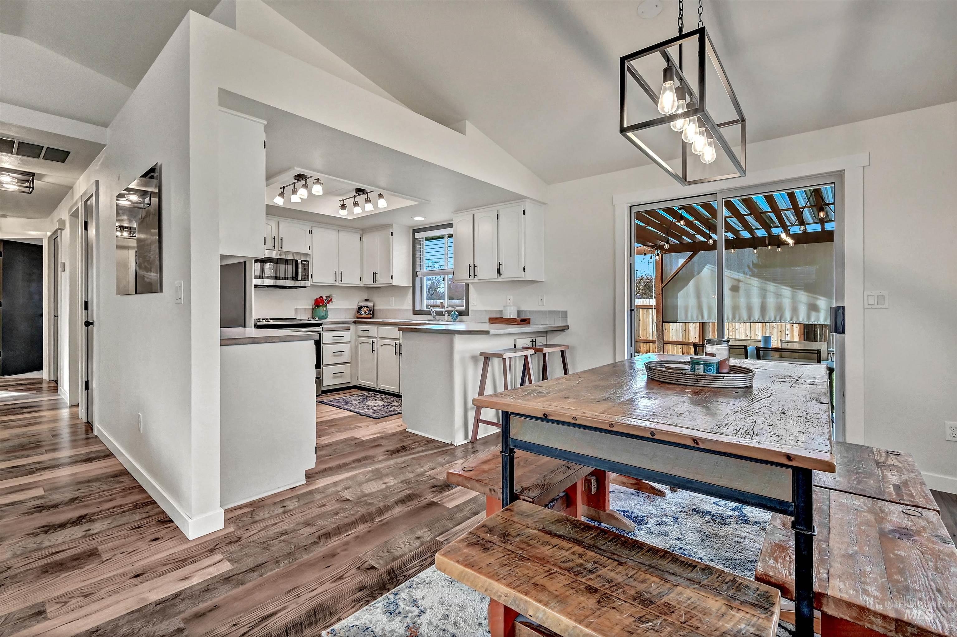 Kitchen with a peninsula, white cabinetry, appliances with stainless steel finishes, decorative light fixtures, and vaulted ceiling