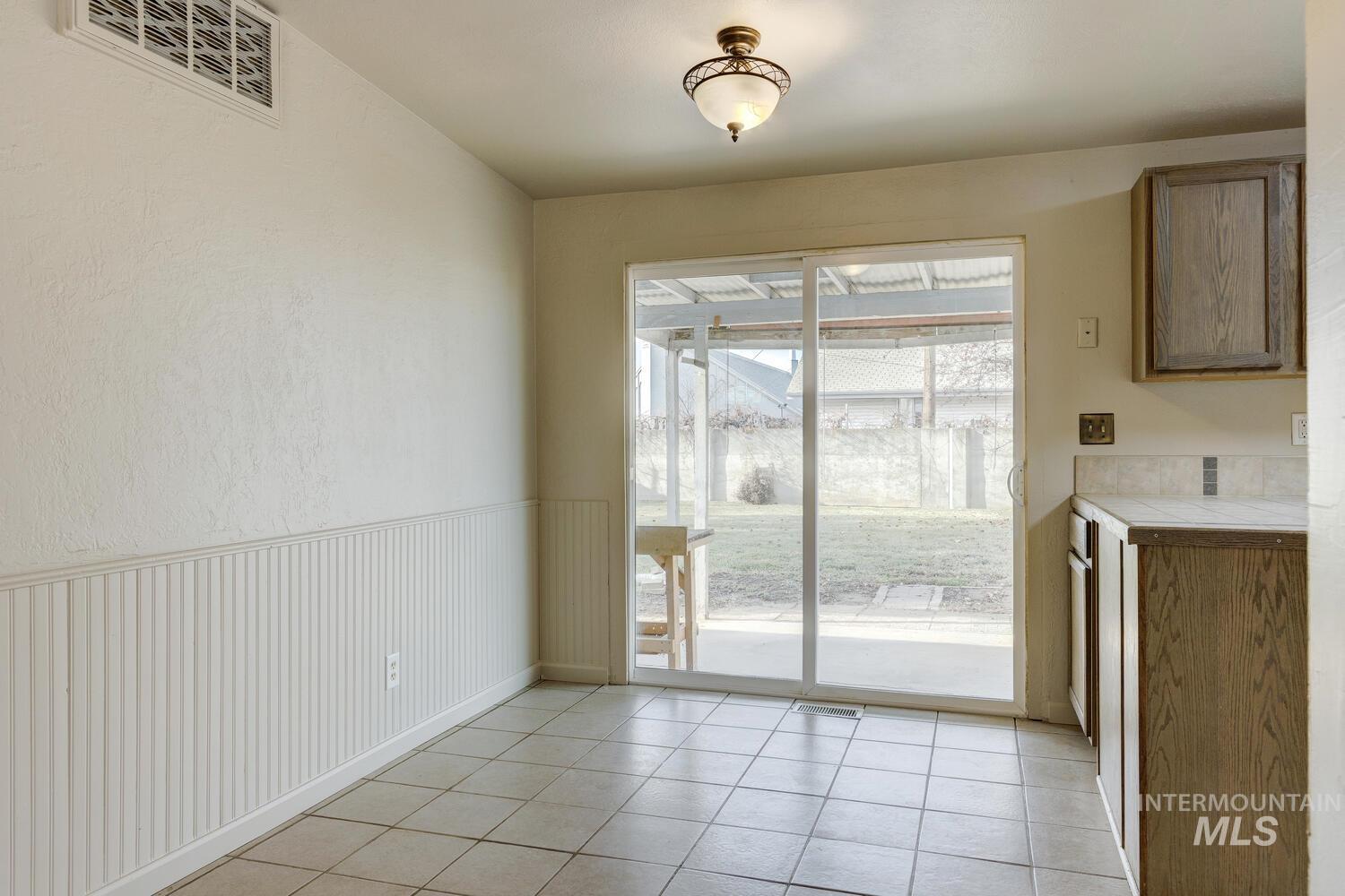 Unfurnished dining area with light tile patterned floors and wainscoting