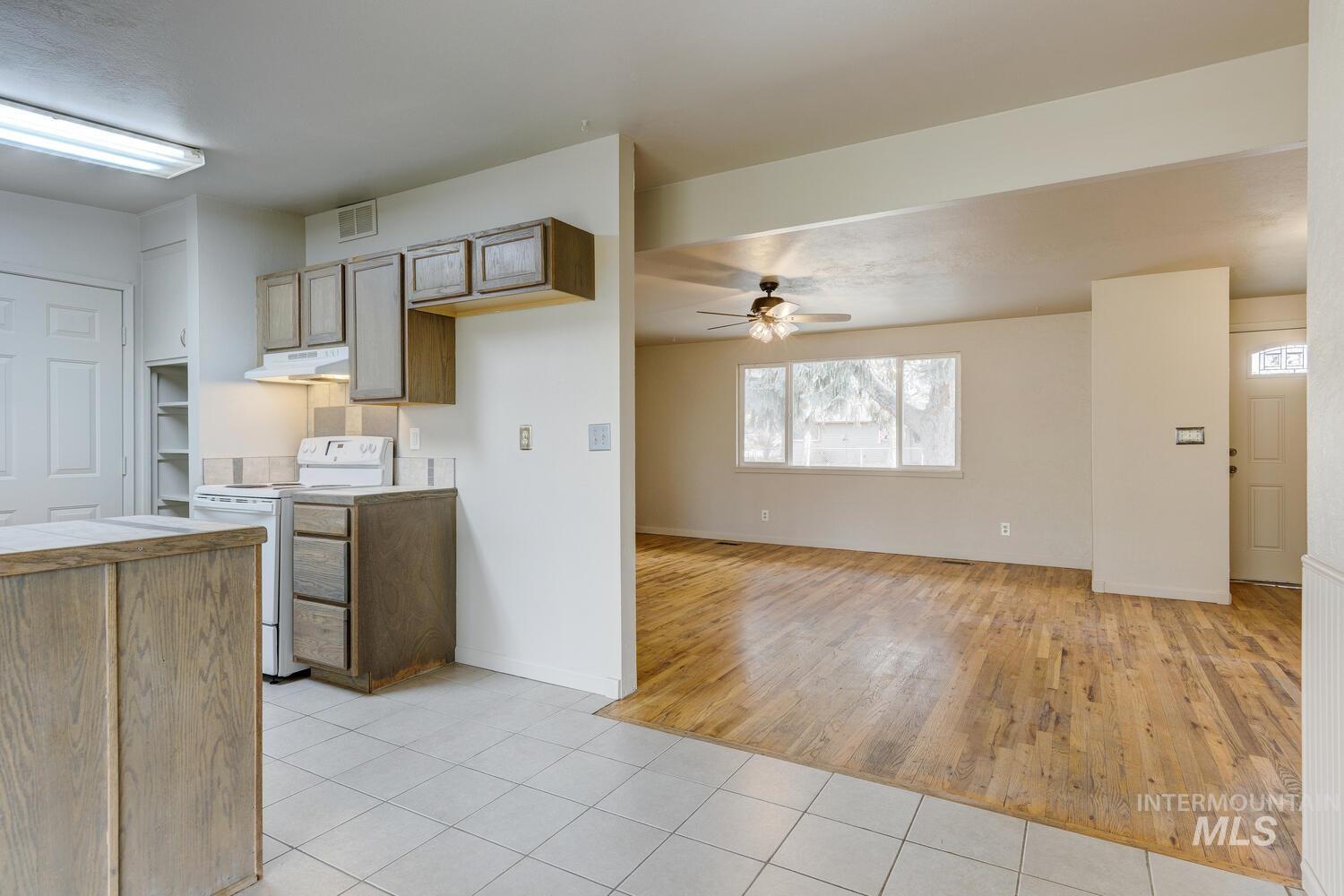 Kitchen with white electric range, light tile patterned flooring, brown cabinets, a ceiling fan, and under cabinet range hood