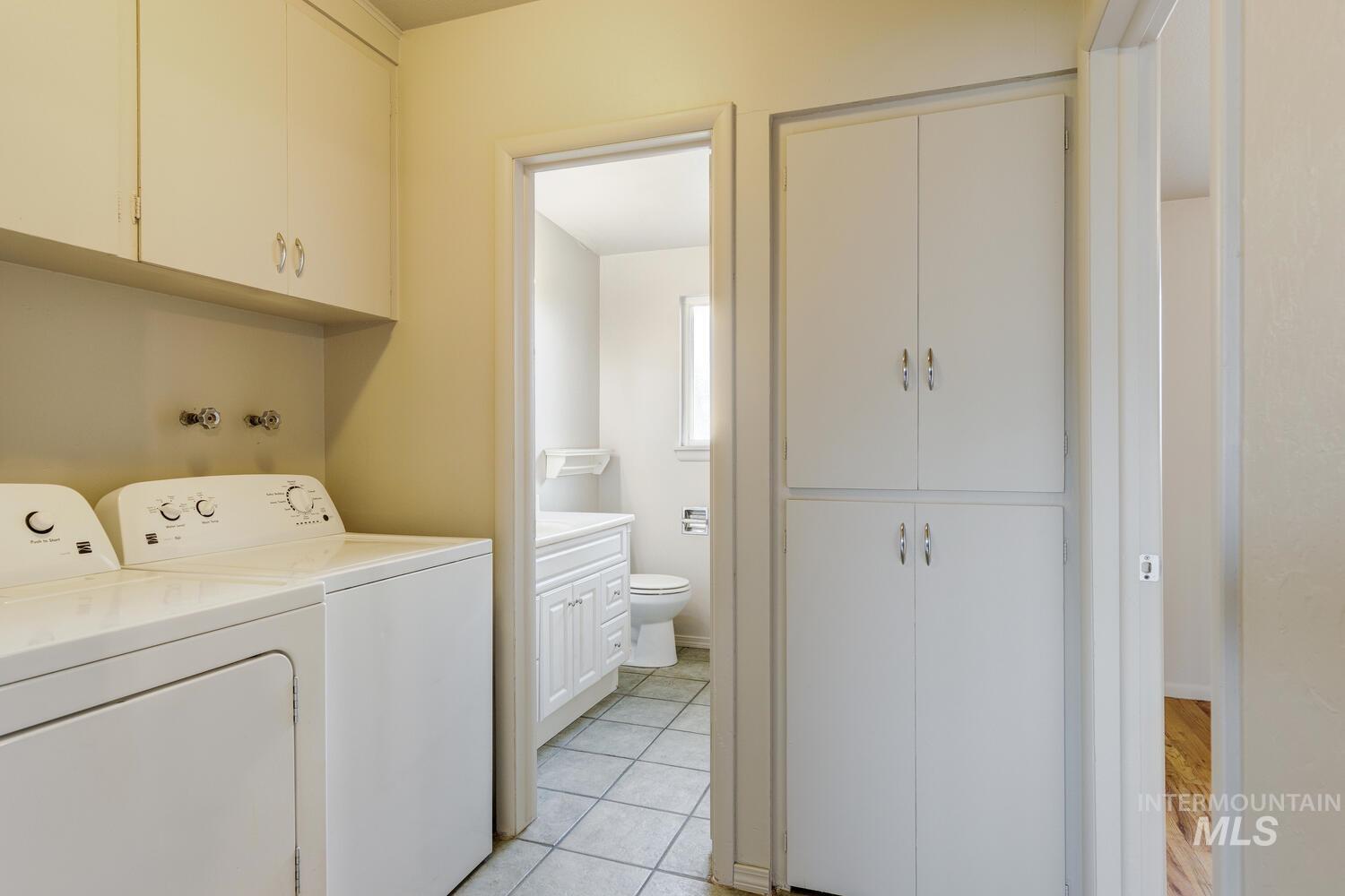 Laundry area featuring washer and clothes dryer, cabinet space, and light tile patterned floors