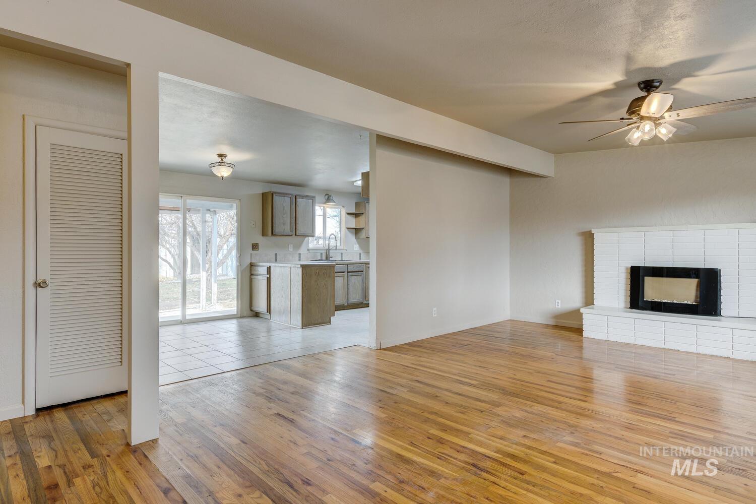Unfurnished living room featuring a brick fireplace, light wood-style flooring, and a ceiling fan