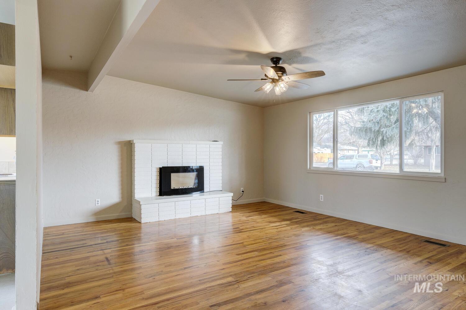 Unfurnished living room with a fireplace, light wood finished floors, a ceiling fan, and beam ceiling