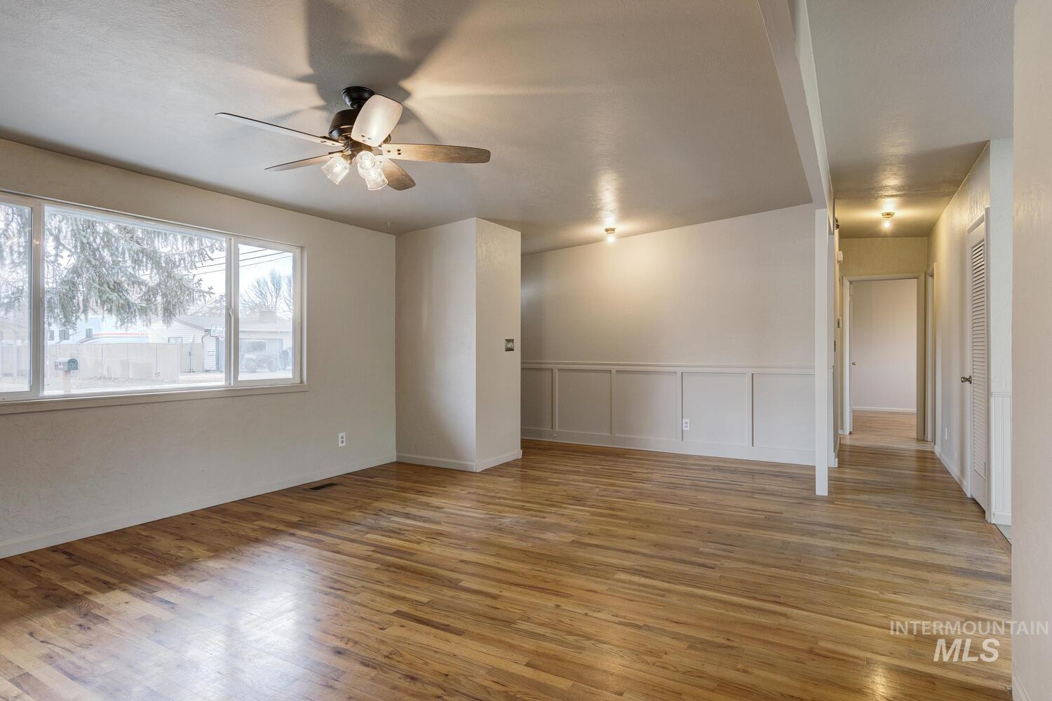 Empty room with light wood finished floors, a ceiling fan, wainscoting, and a decorative wall