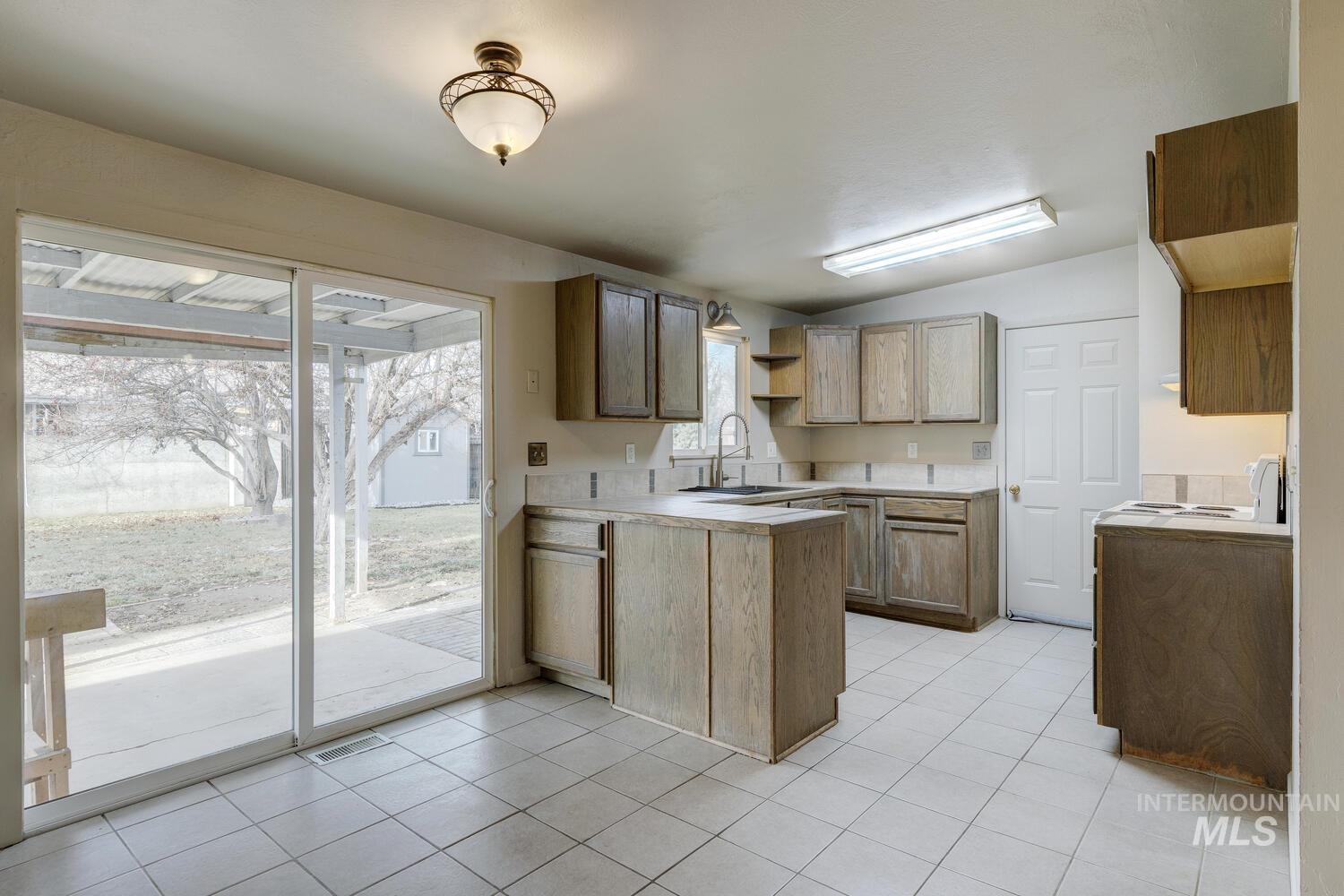 Kitchen featuring lofted ceiling, a peninsula, light countertops, light tile patterned floors, and open shelves