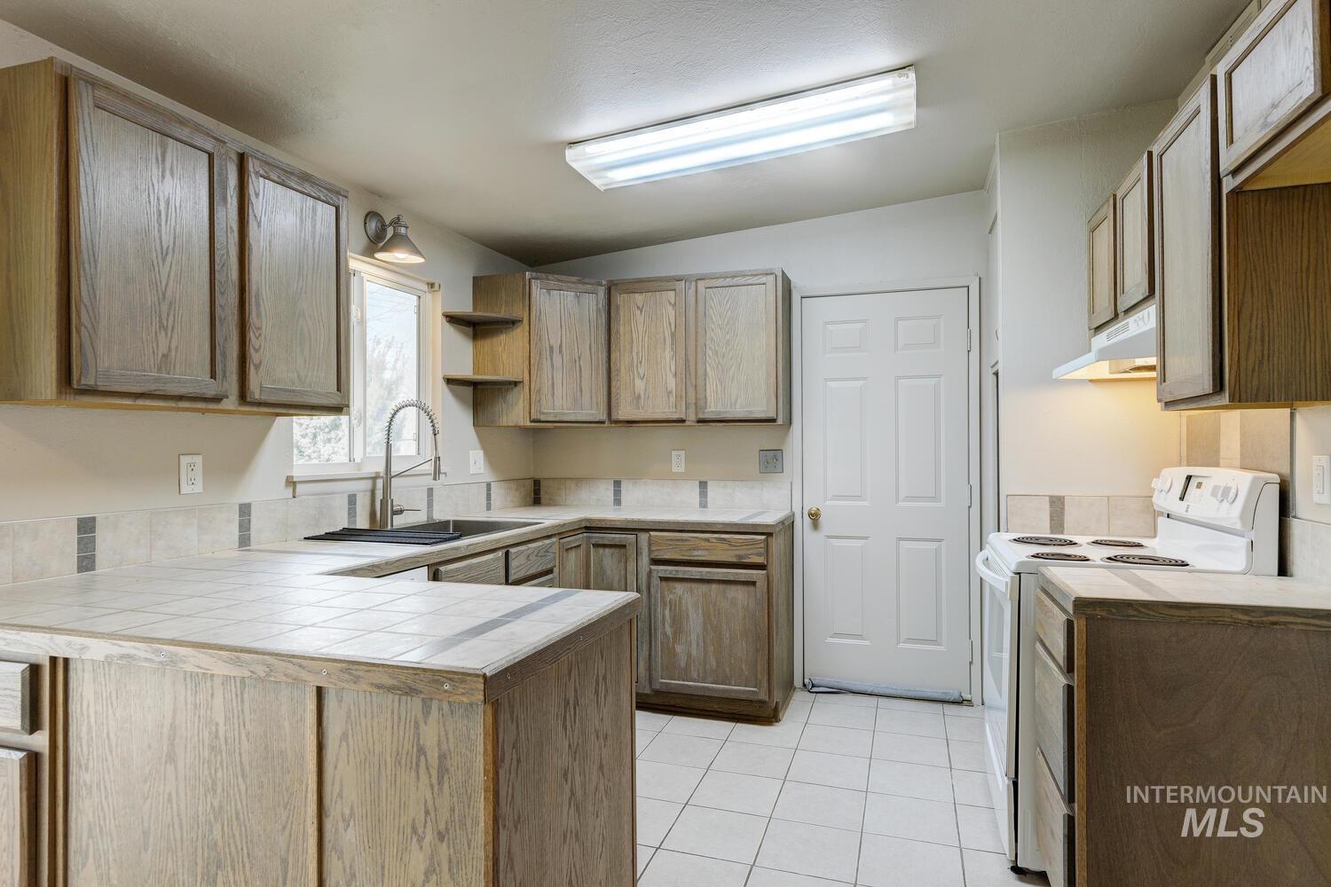 Kitchen featuring white range with electric cooktop, open shelves, a peninsula, lofted ceiling, and tile counters