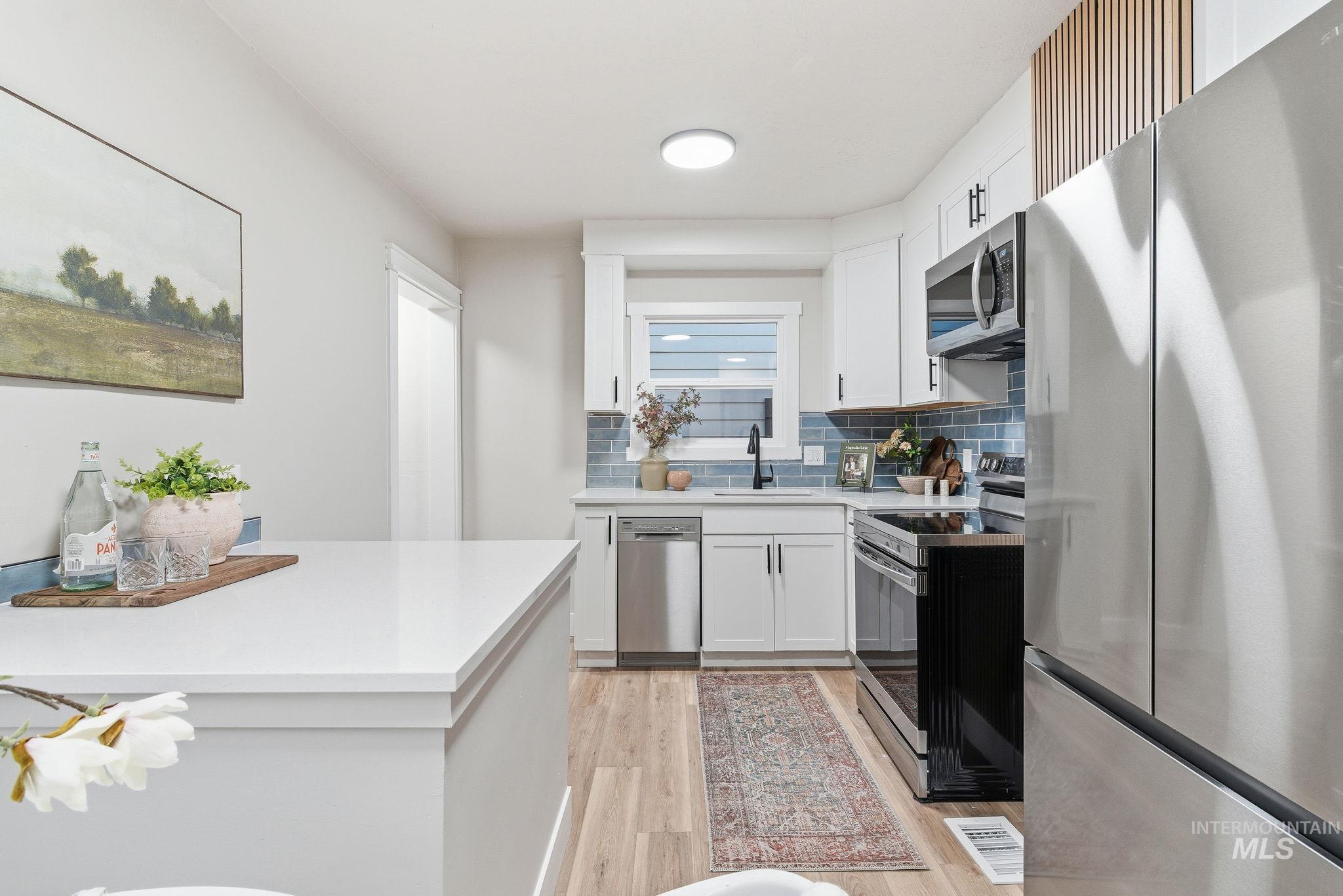 Kitchen with appliances with stainless steel finishes, white cabinets, backsplash, light wood-style floors, and light stone countertops