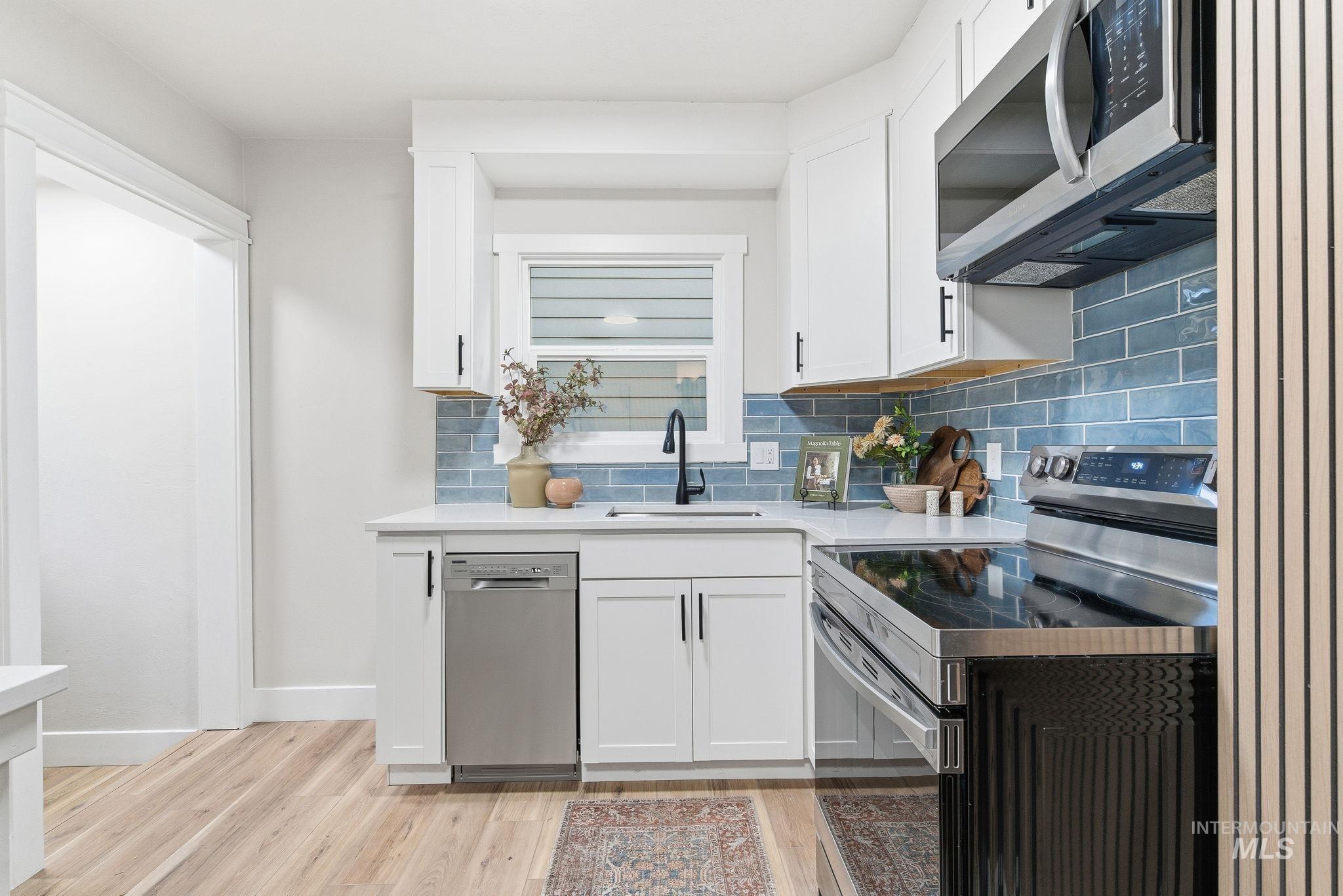 Kitchen featuring appliances with stainless steel finishes, white cabinets, backsplash, and light wood finished floors