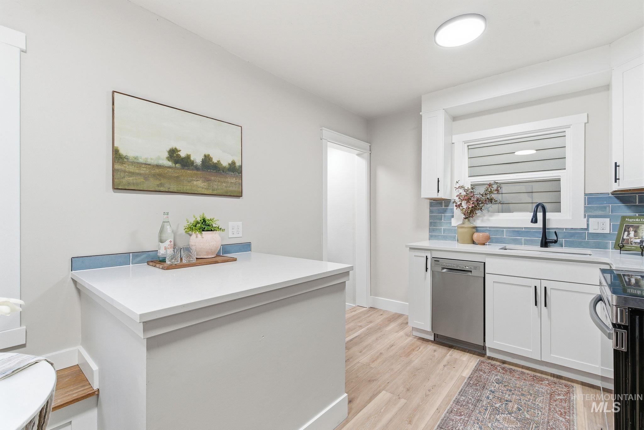 Kitchen with white cabinetry, tasteful backsplash, stainless steel appliances, light wood-type flooring, and light stone countertops