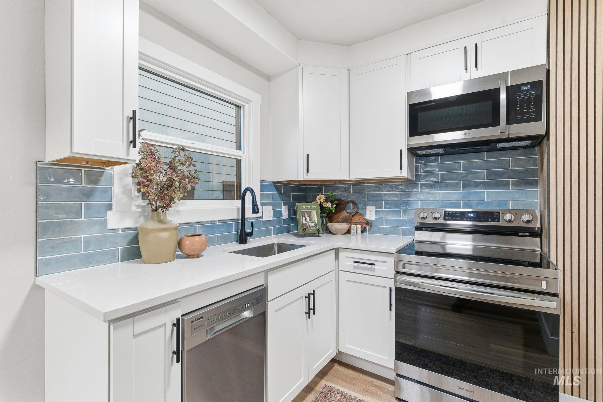 Kitchen featuring stainless steel appliances, white cabinetry, tasteful backsplash, and light stone countertops