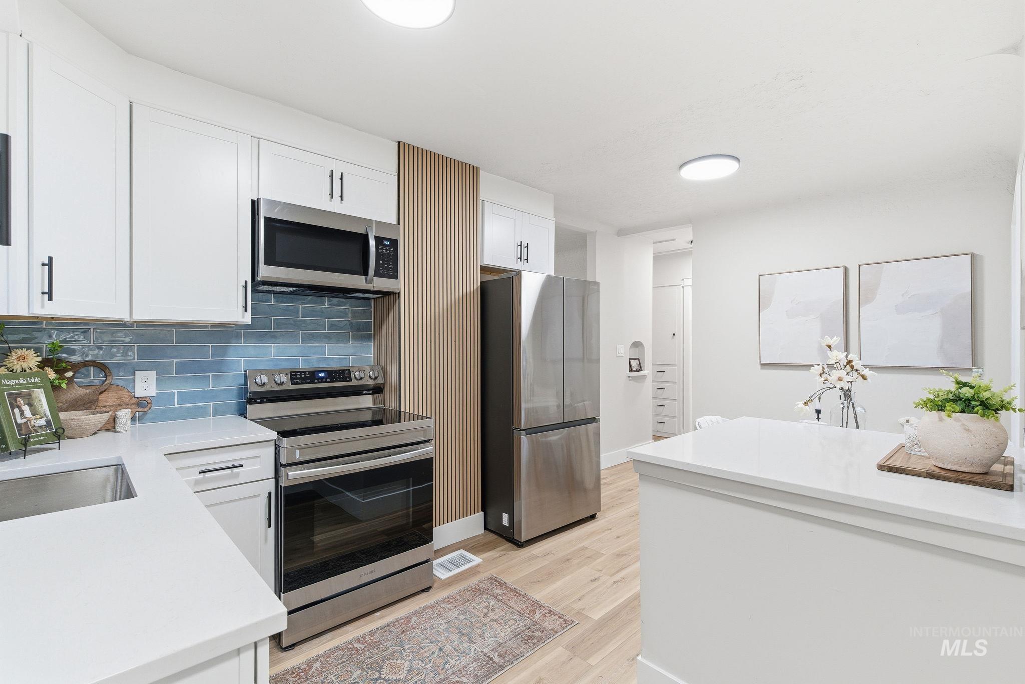 Kitchen featuring appliances with stainless steel finishes, decorative backsplash, white cabinetry, light stone countertops, and light wood finished floors