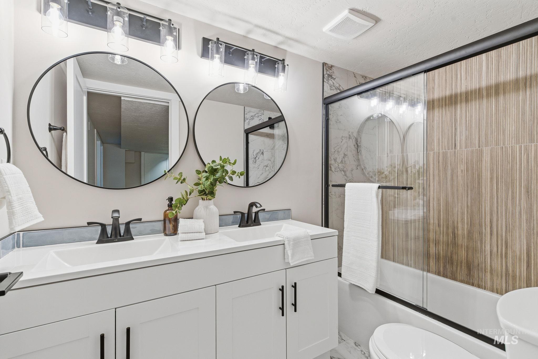 Bathroom featuring double vanity and combined bath / shower with glass door