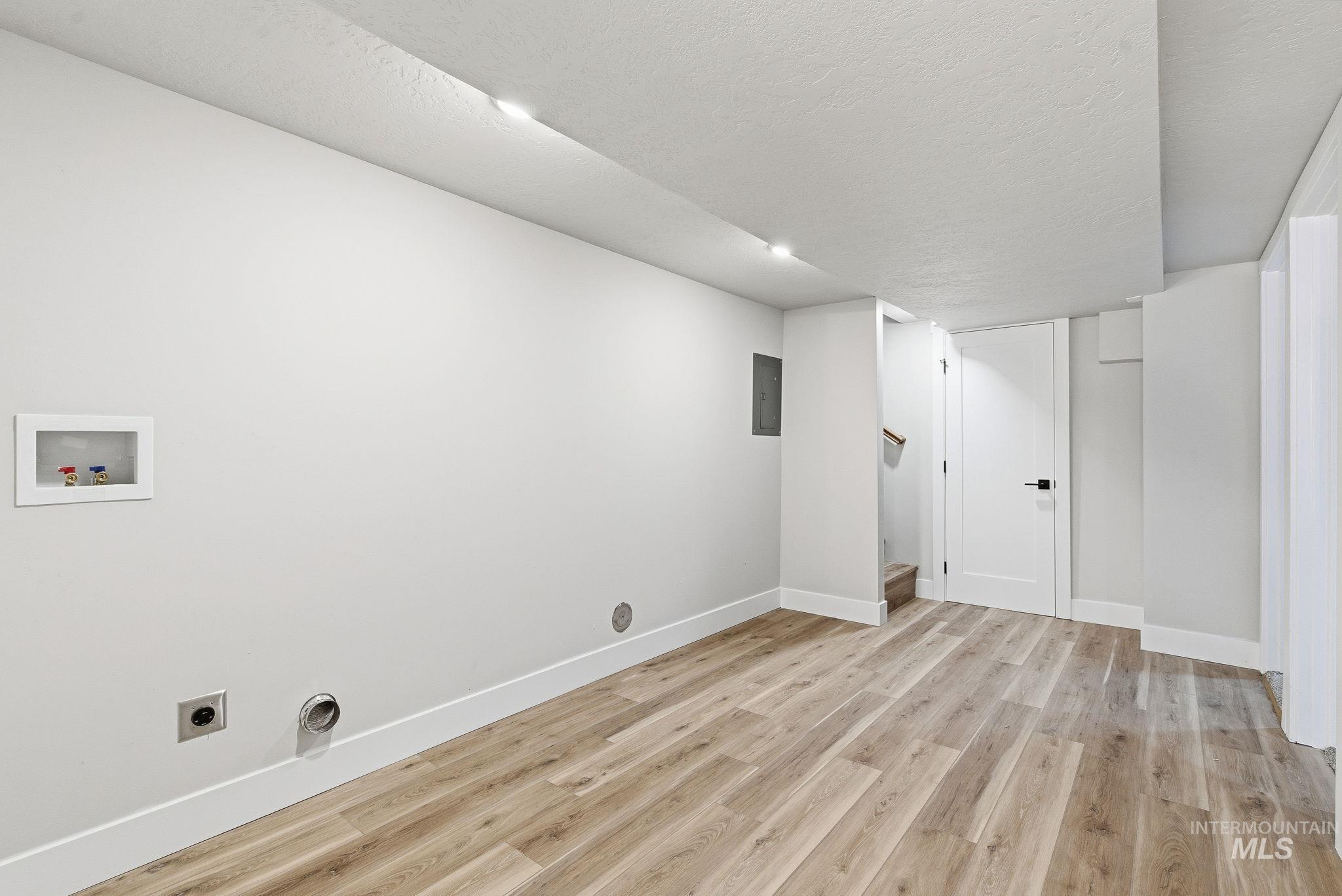 Washroom featuring light wood-type flooring, hookup for a washing machine, a textured ceiling, hookup for an electric dryer, and electric panel