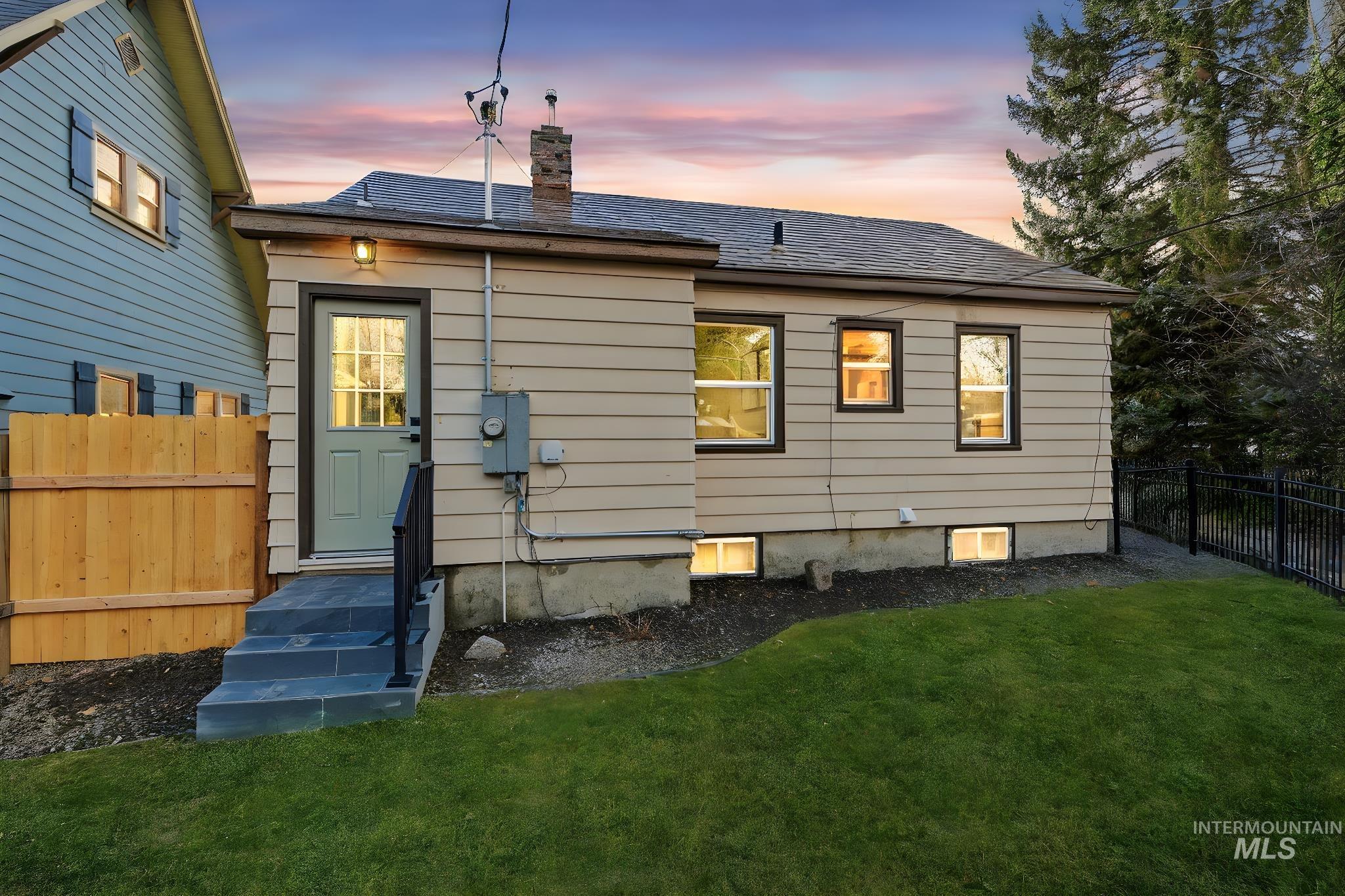 Back of property at dusk featuring a fenced backyard, a chimney, and entry steps
