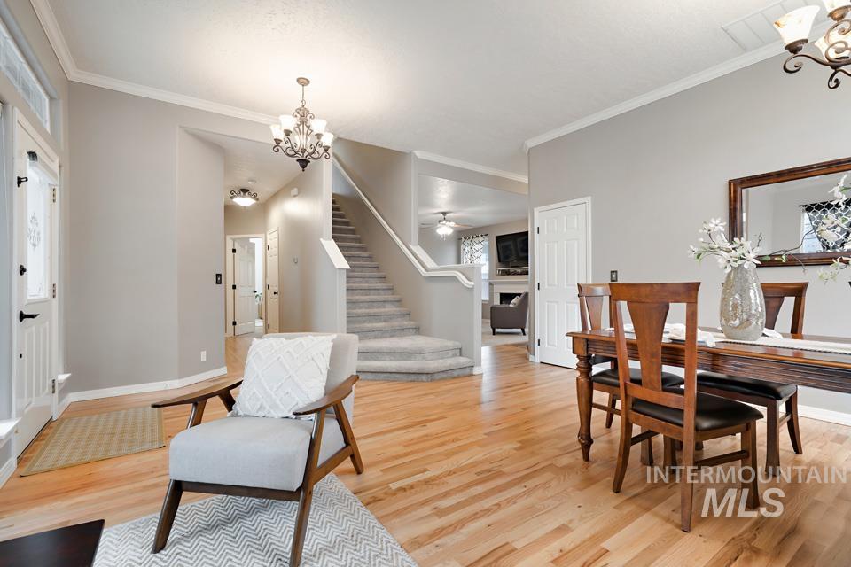 Dining room featuring a chandelier, a fireplace, light wood-style floors, ornamental molding, and stairs