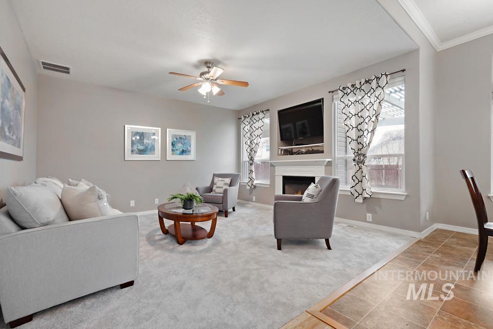 Tiled living area featuring a warm lit fireplace, carpet, plenty of natural light, and ceiling fan