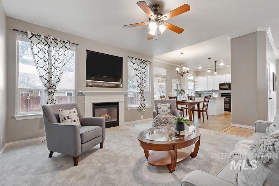 Living room with a glass covered fireplace, a chandelier, ornamental molding, and ceiling fan