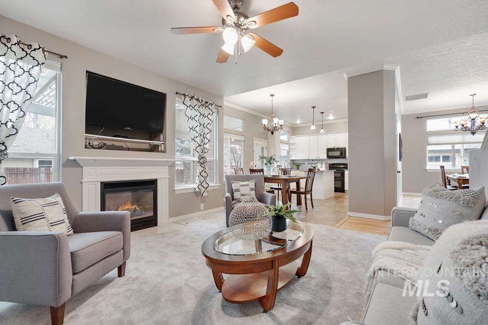 Living room featuring a chandelier, a glass covered fireplace, ceiling fan, and ornamental molding
