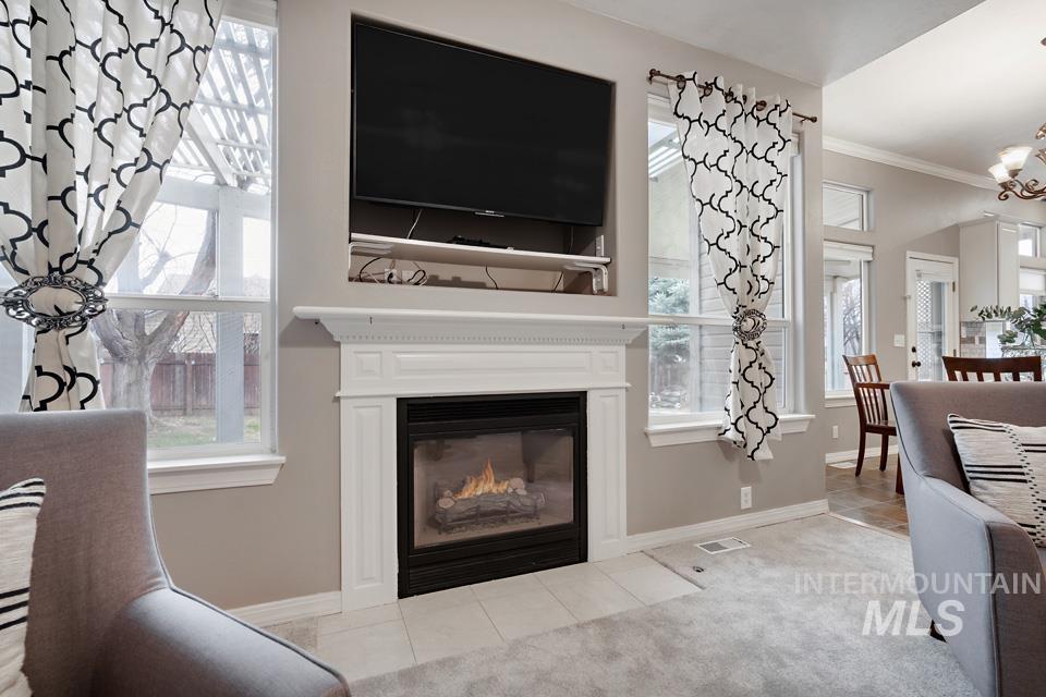 Living area with ornamental molding, light carpet, a fireplace with flush hearth, and a chandelier
