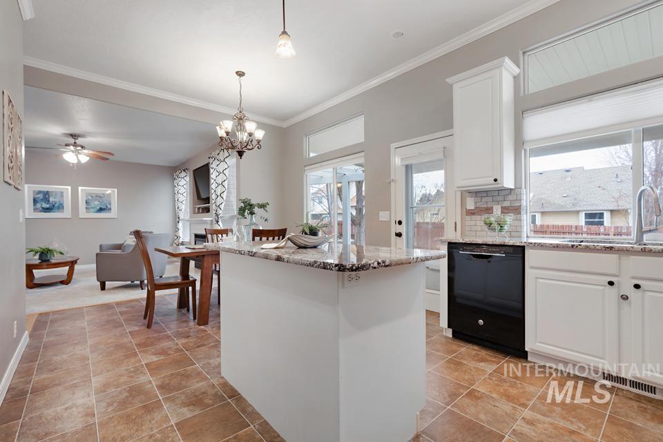 Kitchen featuring white cabinets, light stone countertops, dishwasher, decorative backsplash, and hanging light fixtures
