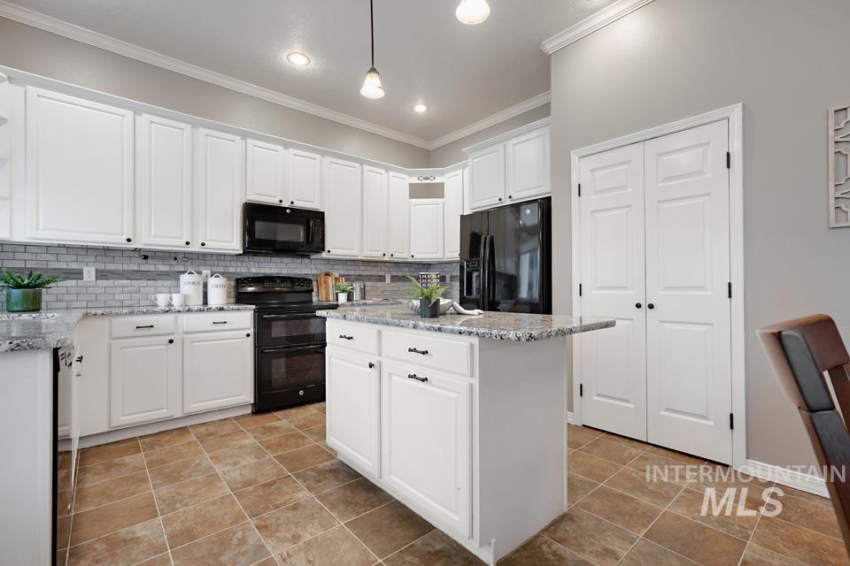 Kitchen with light stone counters, black appliances, white cabinets, a center island, and ornamental molding