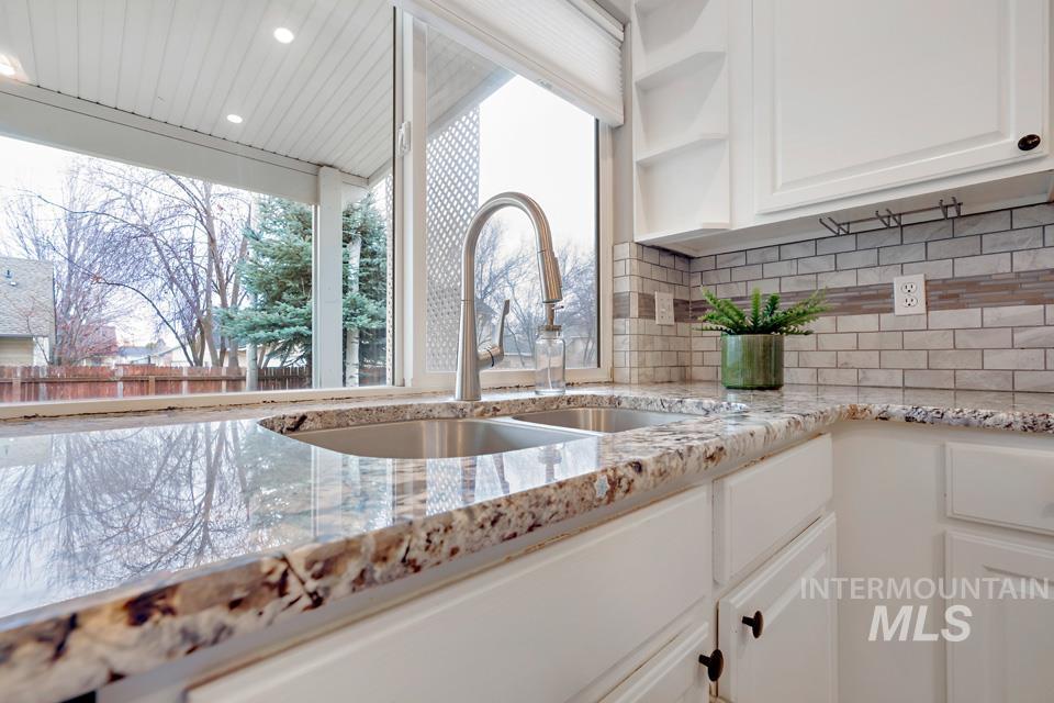 Kitchen with white cabinetry, light stone counters, open shelves, and backsplash