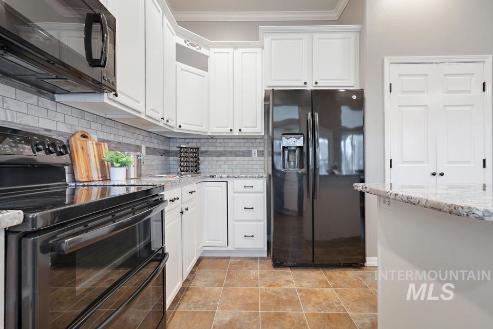 Kitchen with black appliances, tasteful backsplash, light stone counters, white cabinets, and ornamental molding