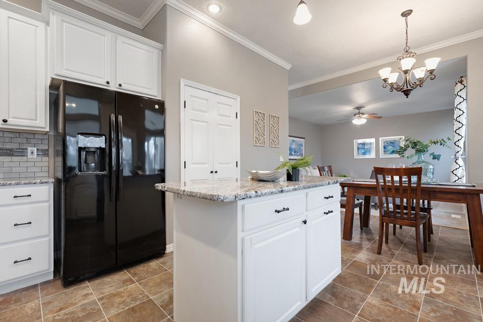 Kitchen featuring white cabinets, black fridge with ice dispenser, a kitchen island, pendant lighting, and crown molding