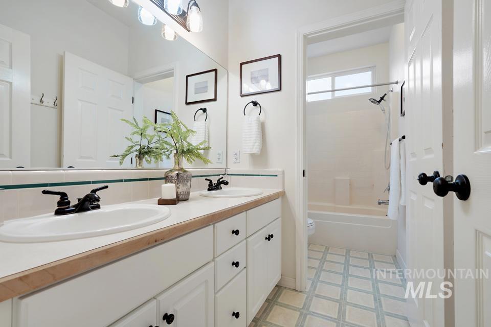 Full bath featuring double vanity, washtub / shower combination, and light floors