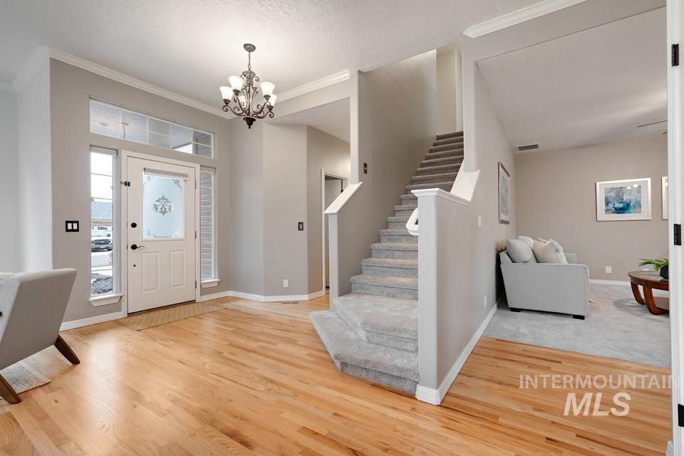Entrance foyer with stairs, crown molding, light wood-type flooring, and a chandelier
